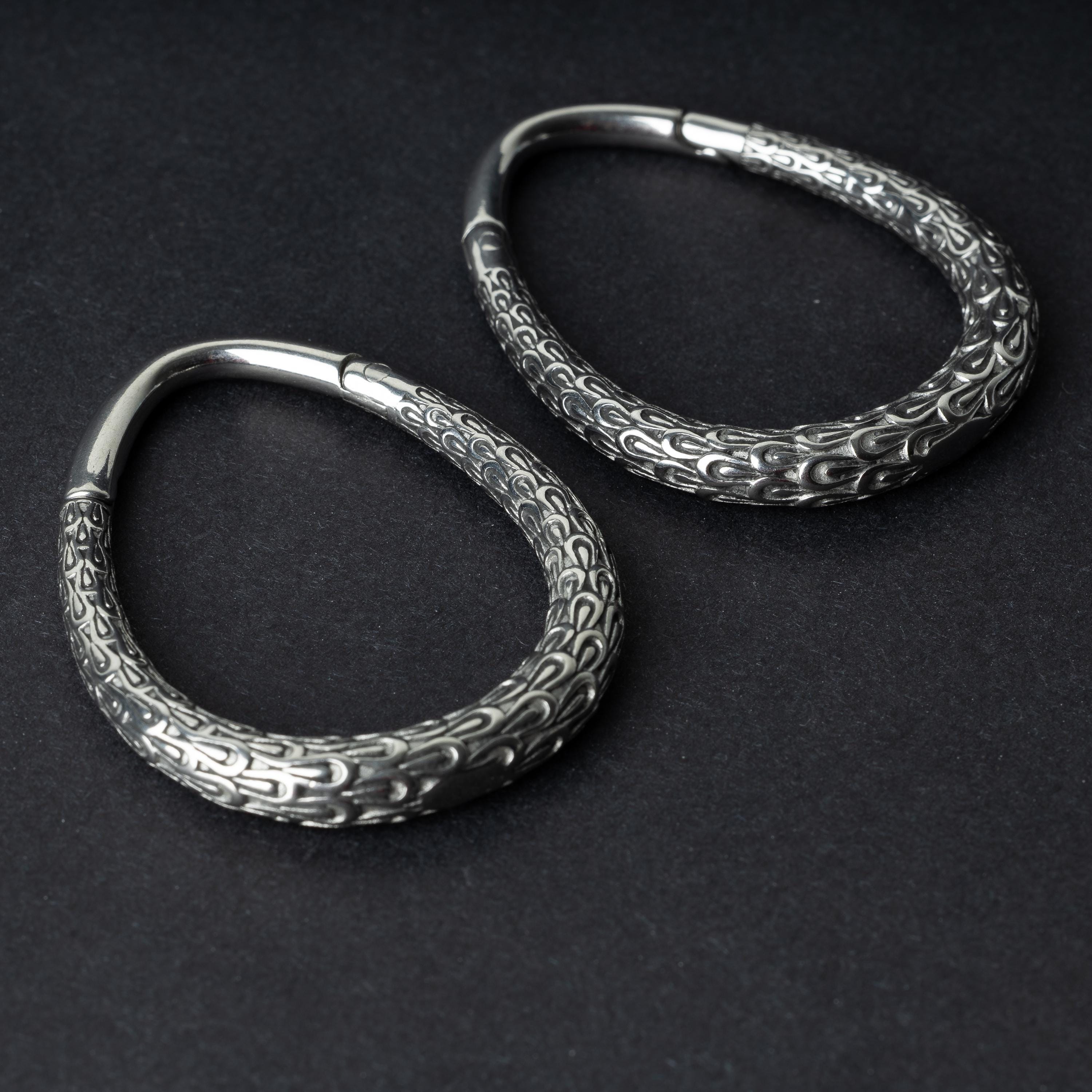 A pair of silver teardrop ear weights featuring a detailed dragon-scale texture and a seamless hinge closure, displayed on a dark background.