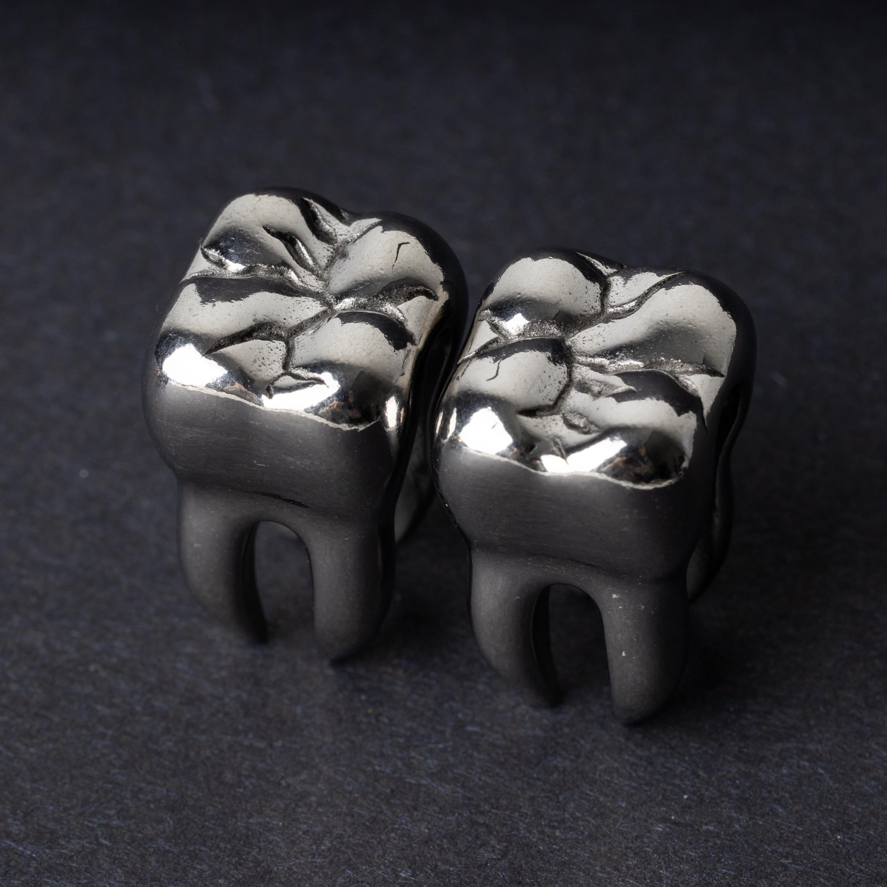 Close-up of silver tooth-shaped ear weights with polished detailing, displayed on a dark background.
