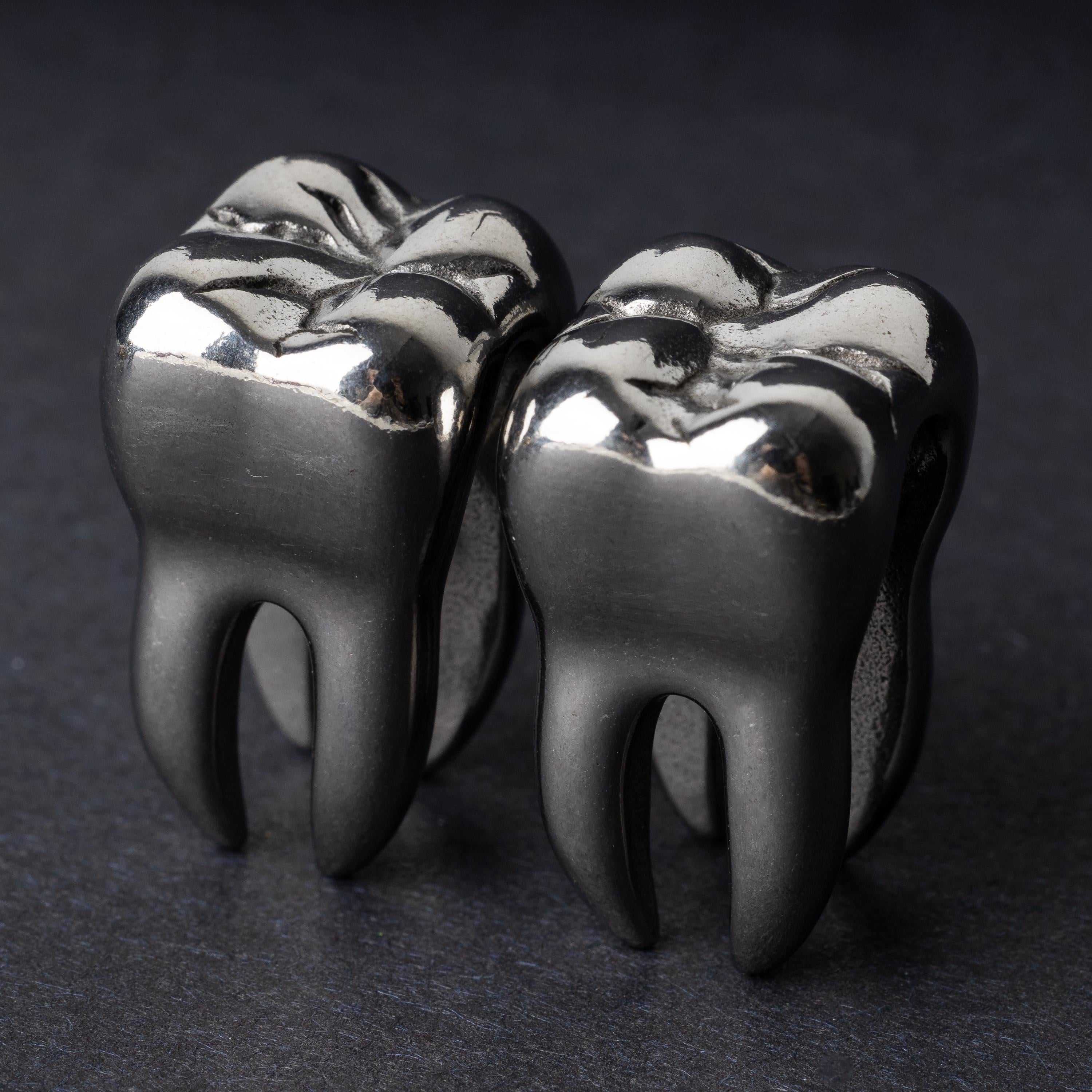 Close-up of silver tooth-shaped ear weights with polished detailing, displayed on a dark background.