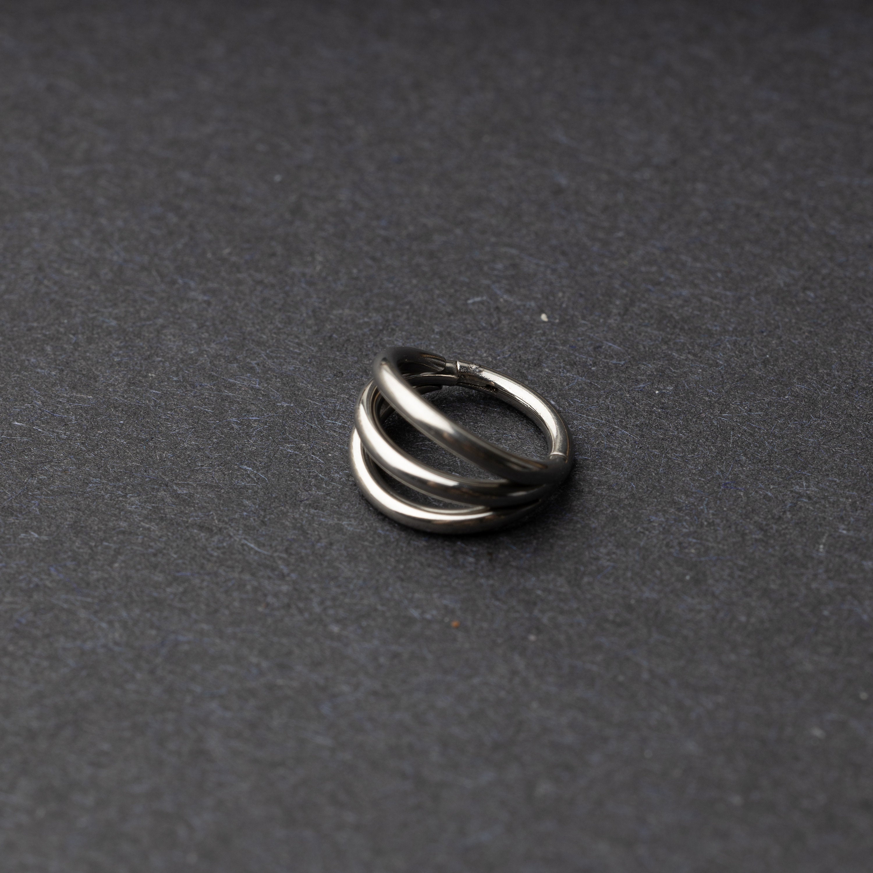 Four triple-band hoop septum clicker ring in silver finish, displayed on a dark background.