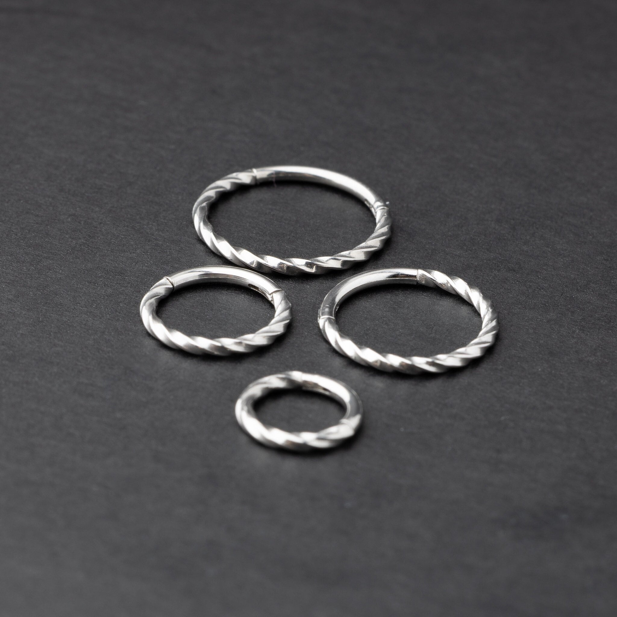 Four stainless steel twisted hoops in different sizes displayed on a dark background, emphasizing their intricate twisted texture.