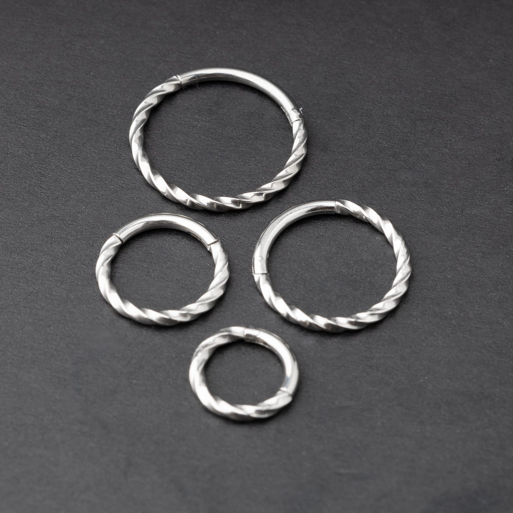 Four stainless steel twisted hoops in different sizes displayed on a dark background, emphasizing their intricate twisted texture.