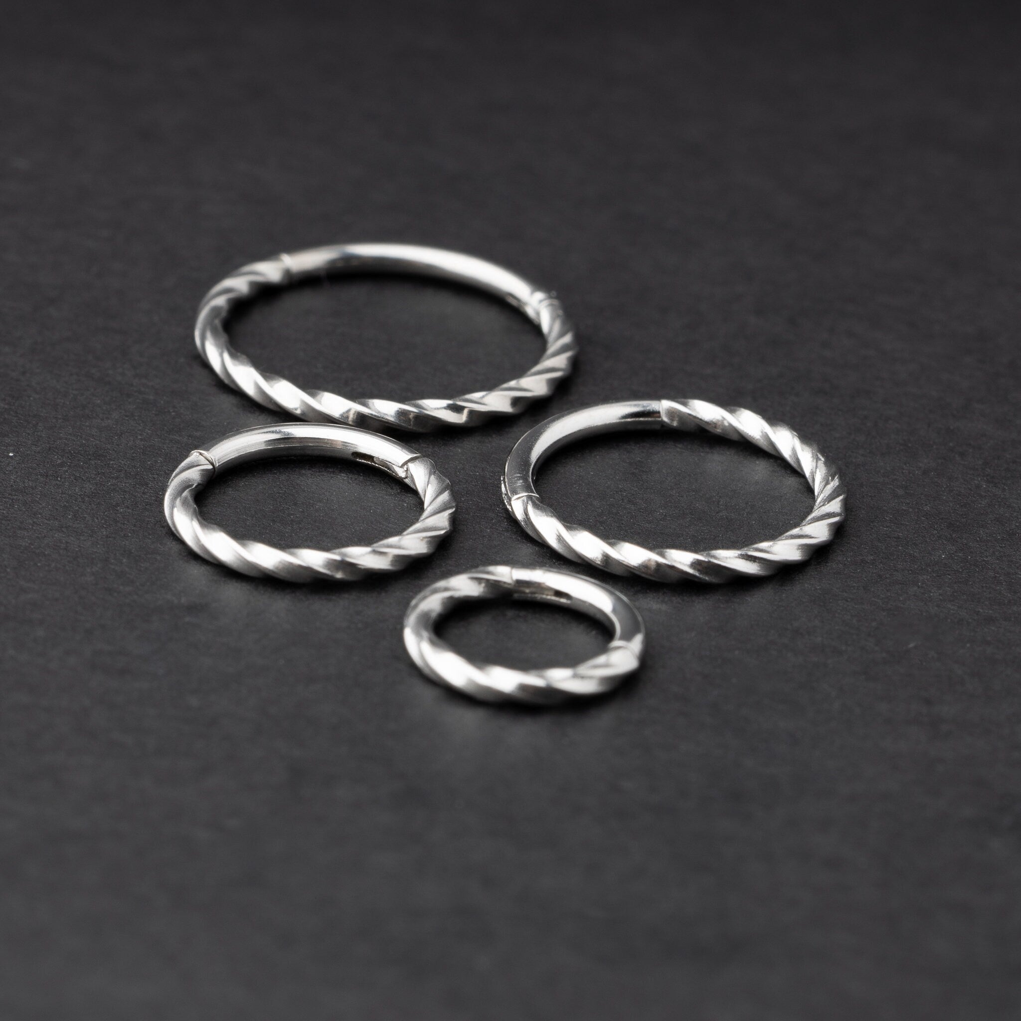 Four stainless steel twisted hoops in different sizes displayed on a dark background, emphasizing their intricate twisted texture.