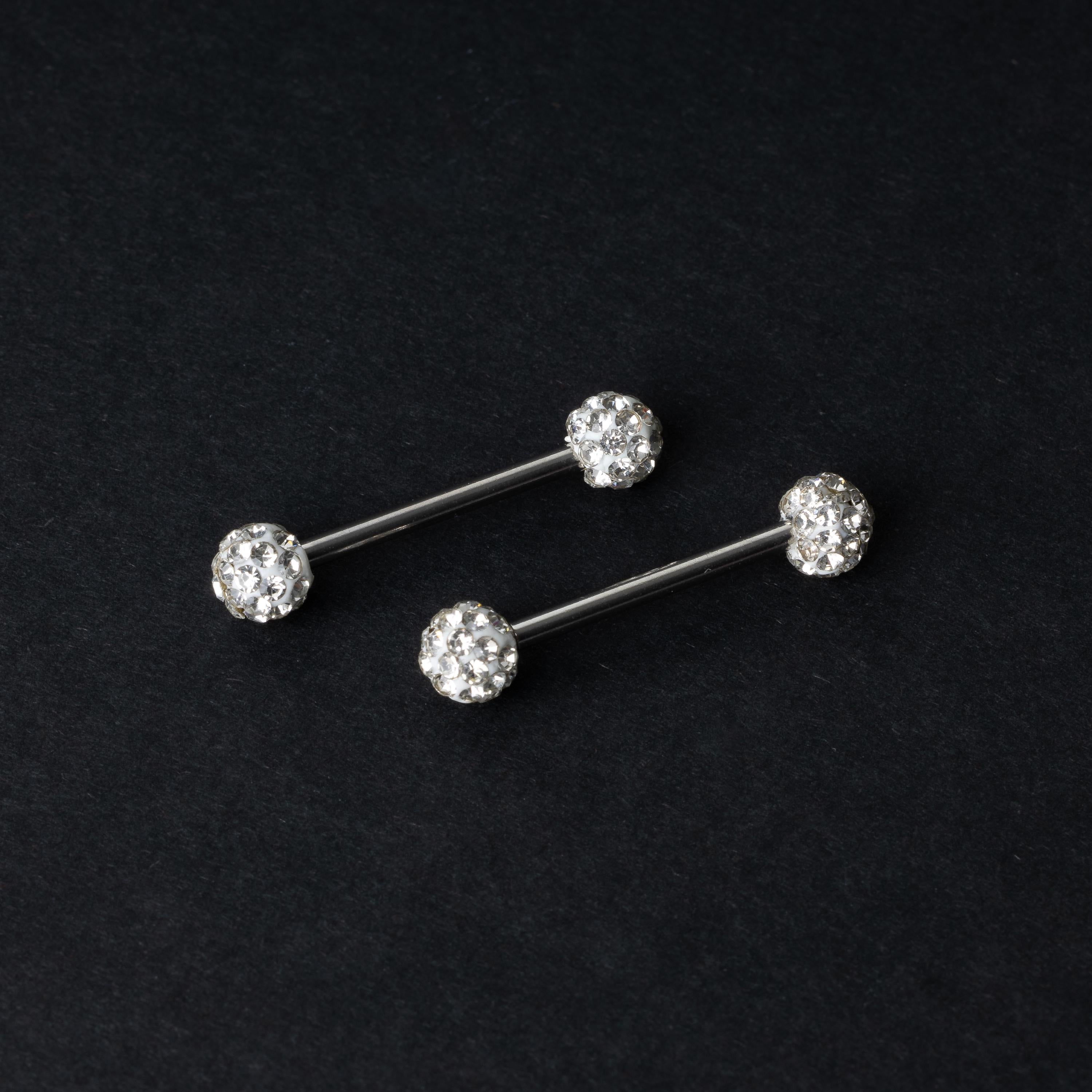 Barbells with textured crystal-encrusted ends in silver displayed on a dark background.