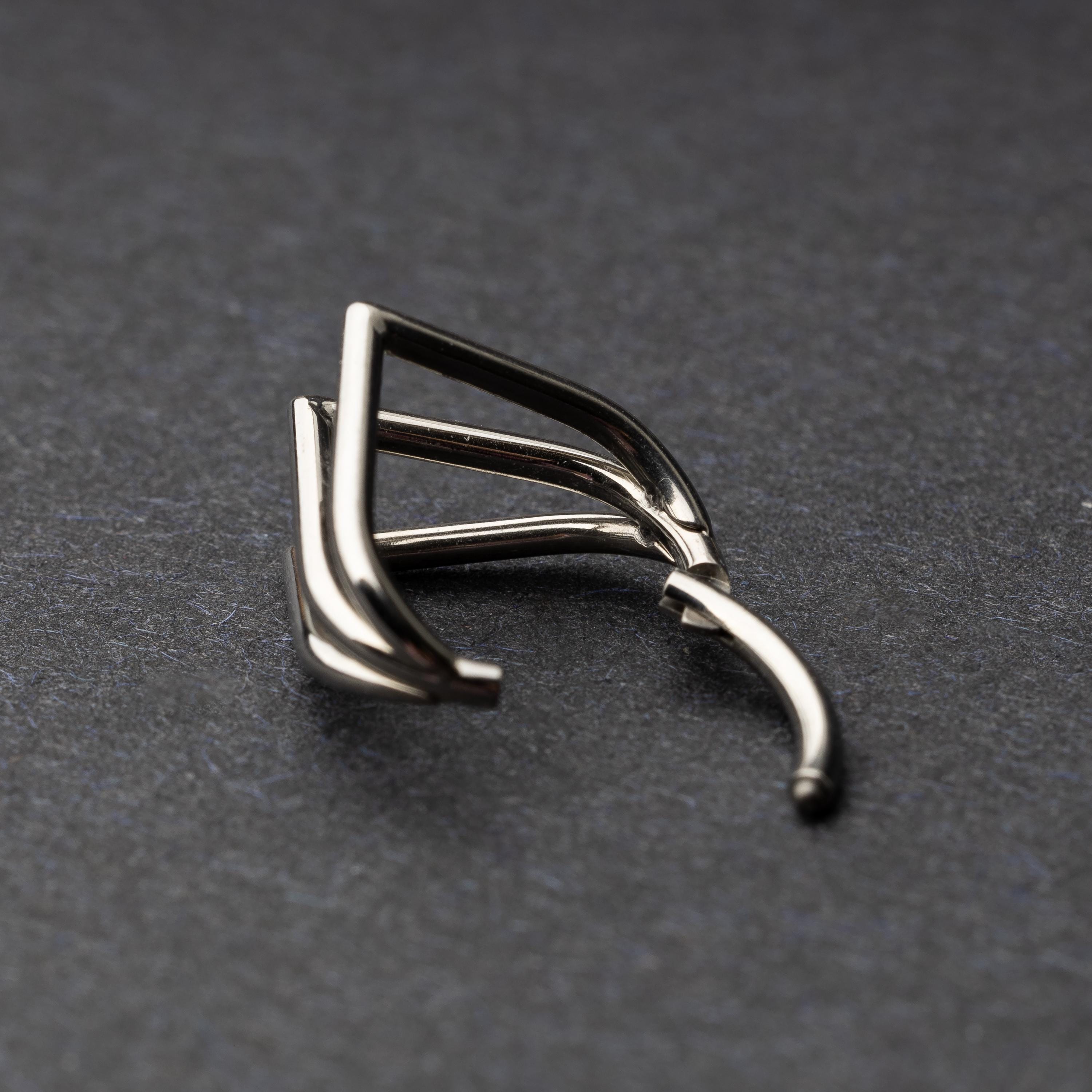 Close-up of a geometric septum clicker in silver, featuring a unique layered triangular design, displayed on a dark background.