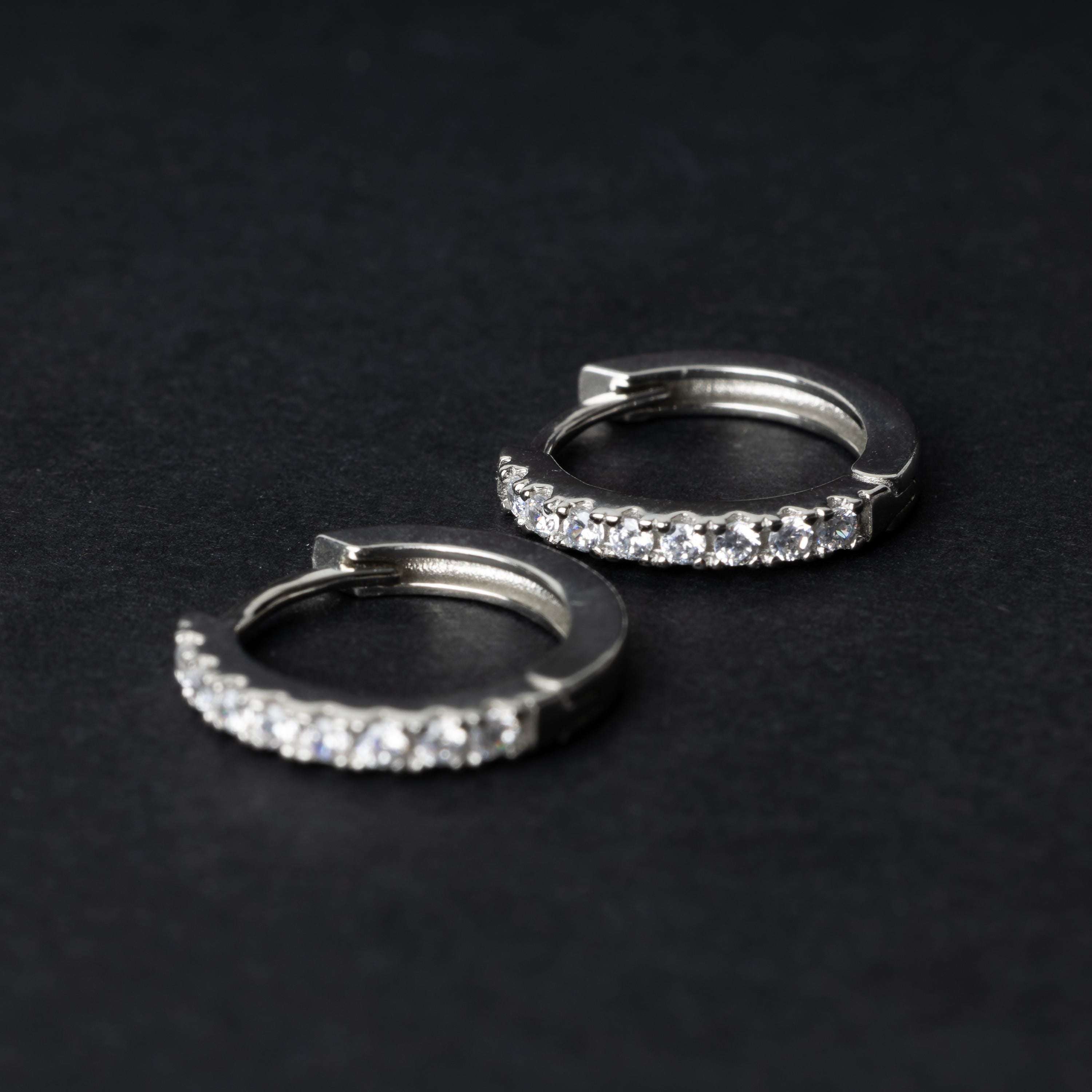 A pair of silver hoop earrings adorned with a row of sparkling cubic zirconia gems, displayed on a black background.