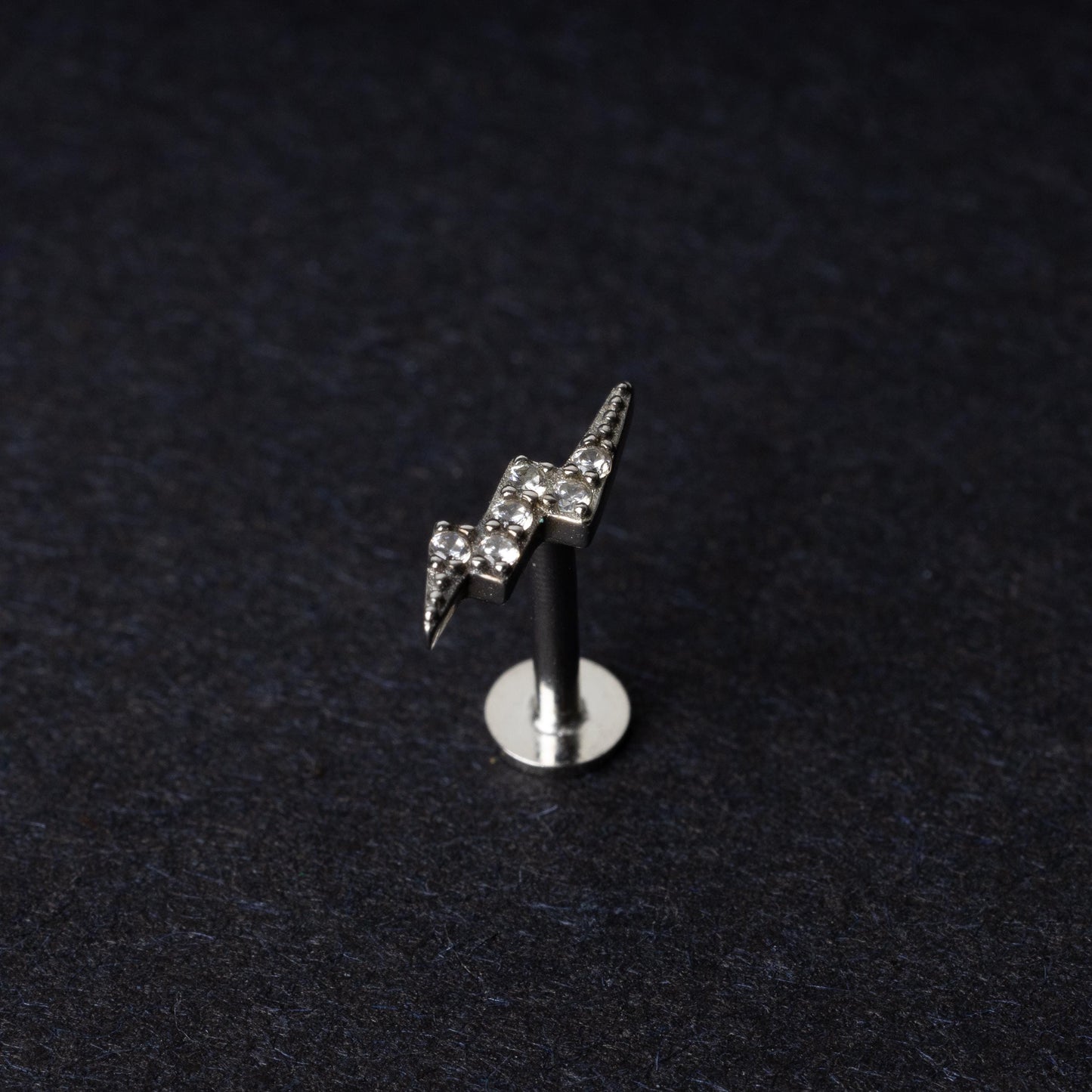 Silver lightning bolt labret stud with crystal detailing, displayed on a dark background.
