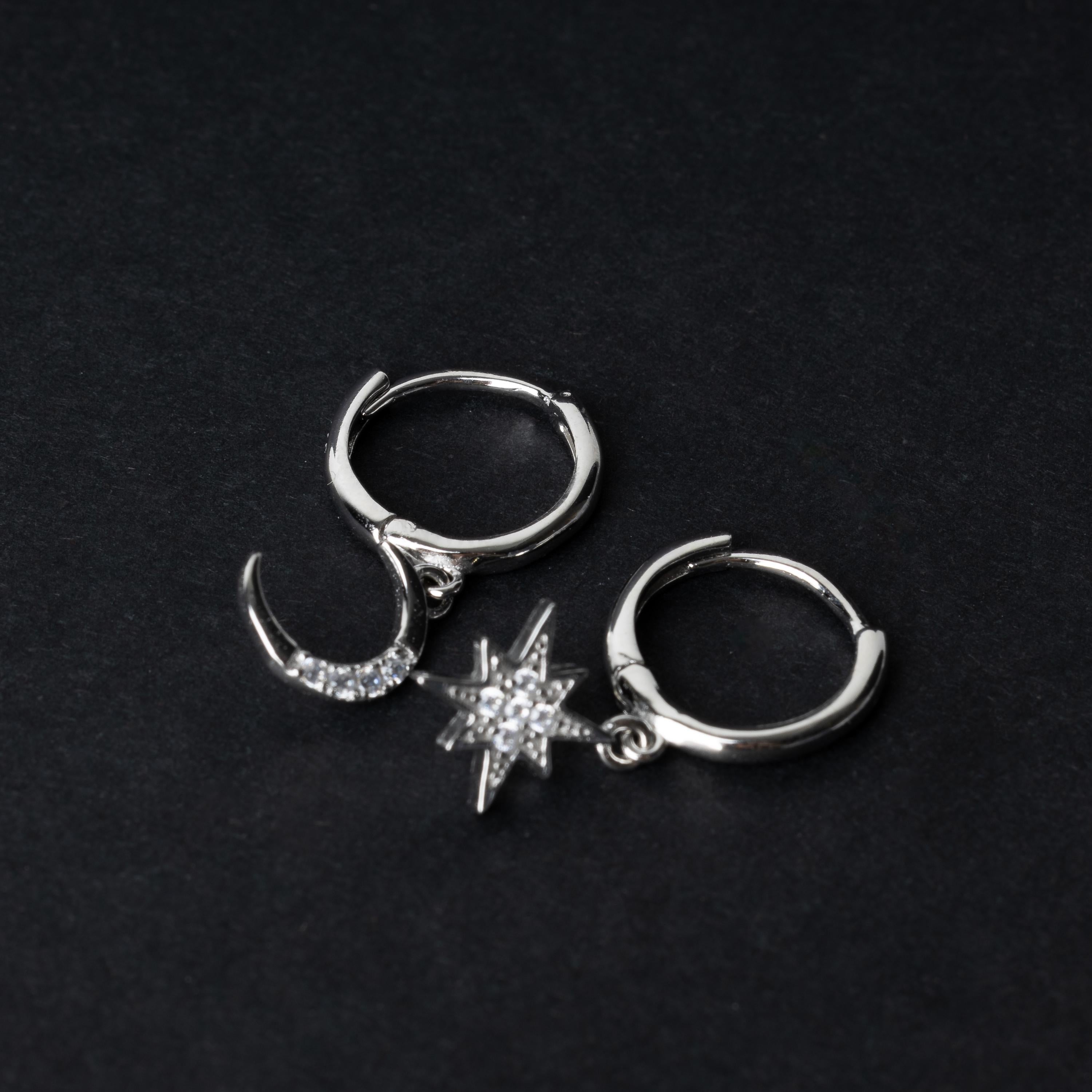 Silver moon and star hoop earrings with cubic zirconia accents, displayed on a dark background.
