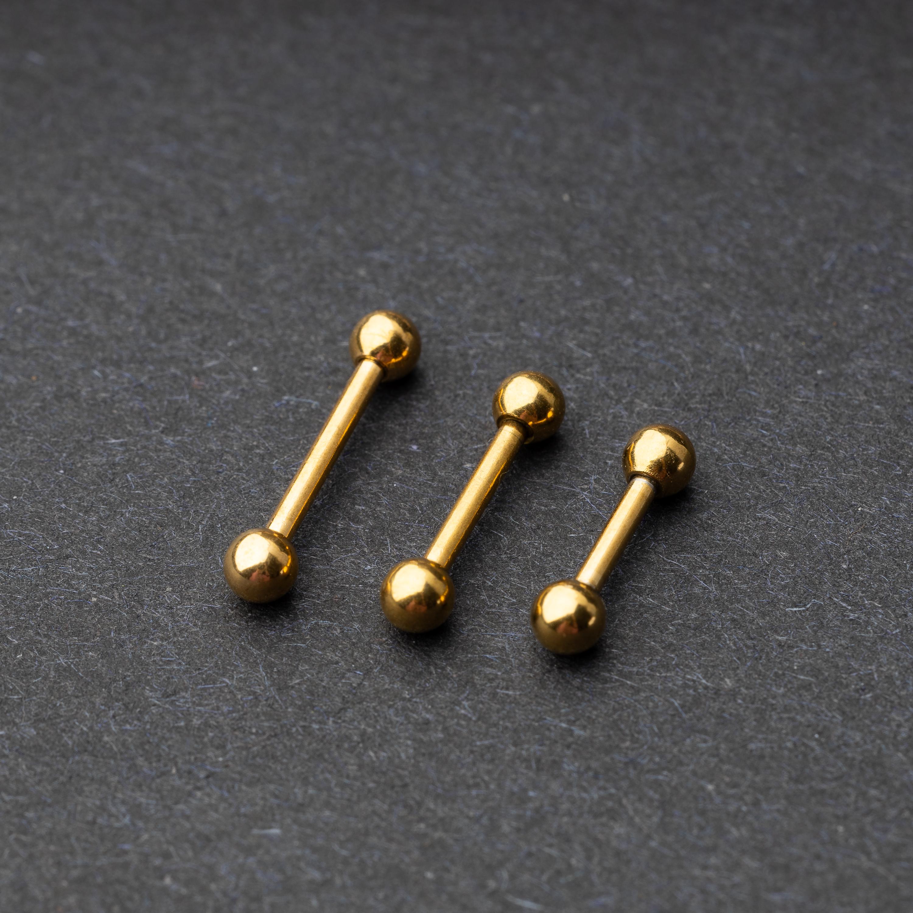 Gold-tone stainless steel barbells with polished spheres on a dark background.