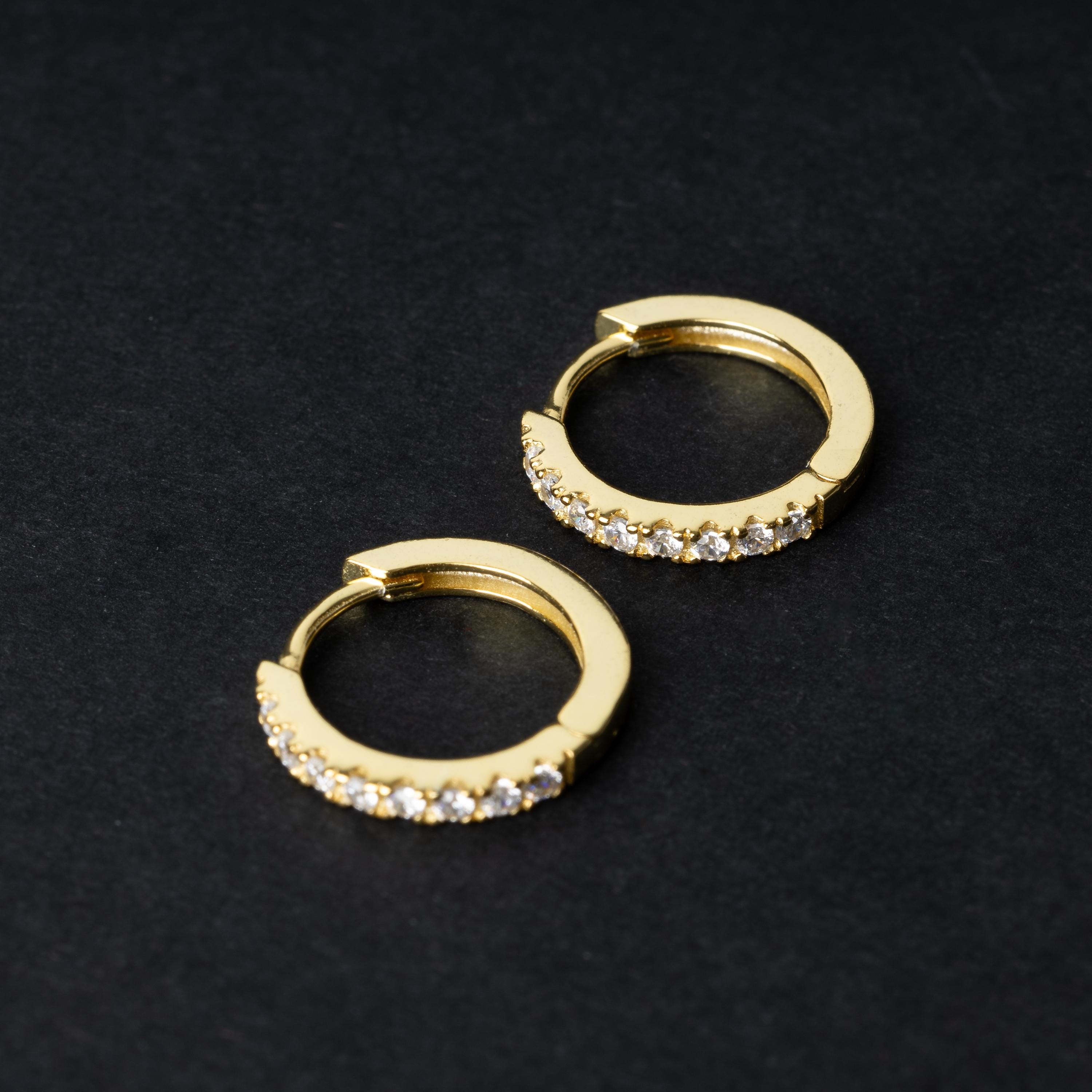 A pair of gold hoop earrings adorned with a row of sparkling cubic zirconia gems, displayed on a black background.