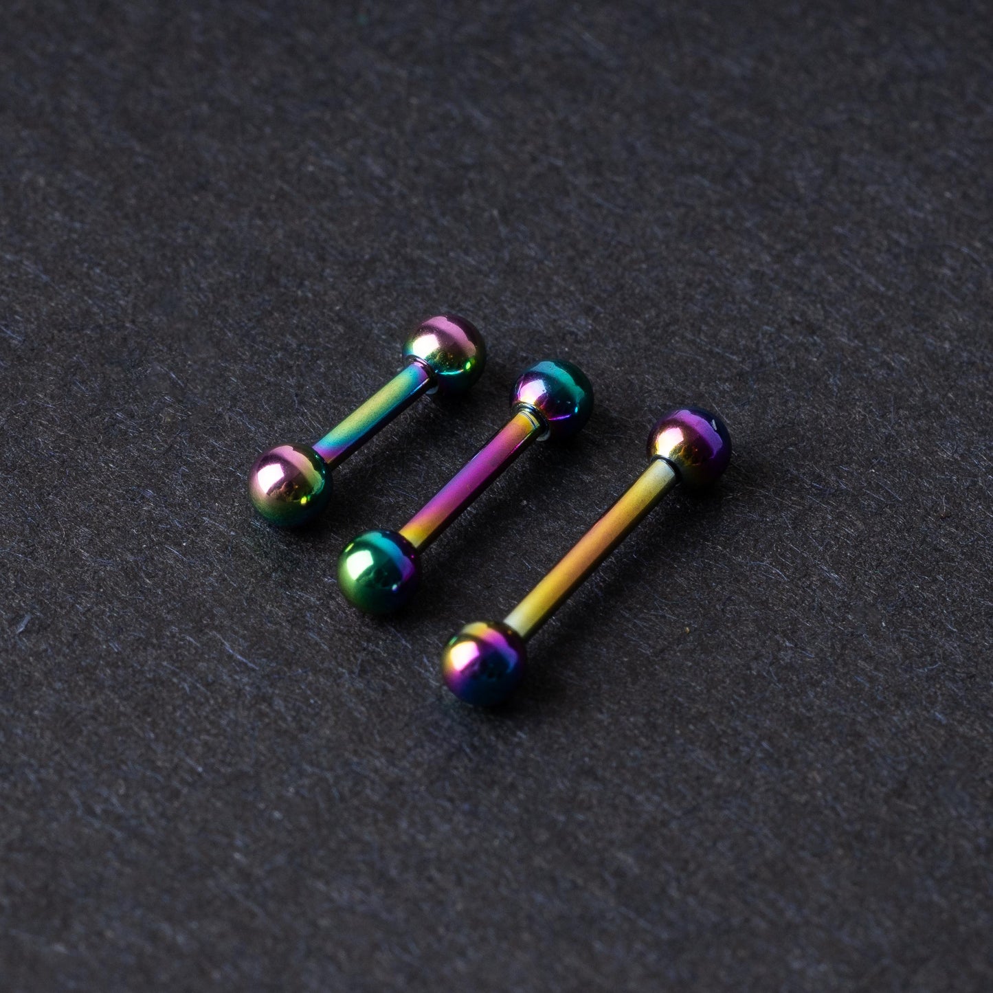 Rainbow stainless steel barbells with an anodized finish on a dark background.
