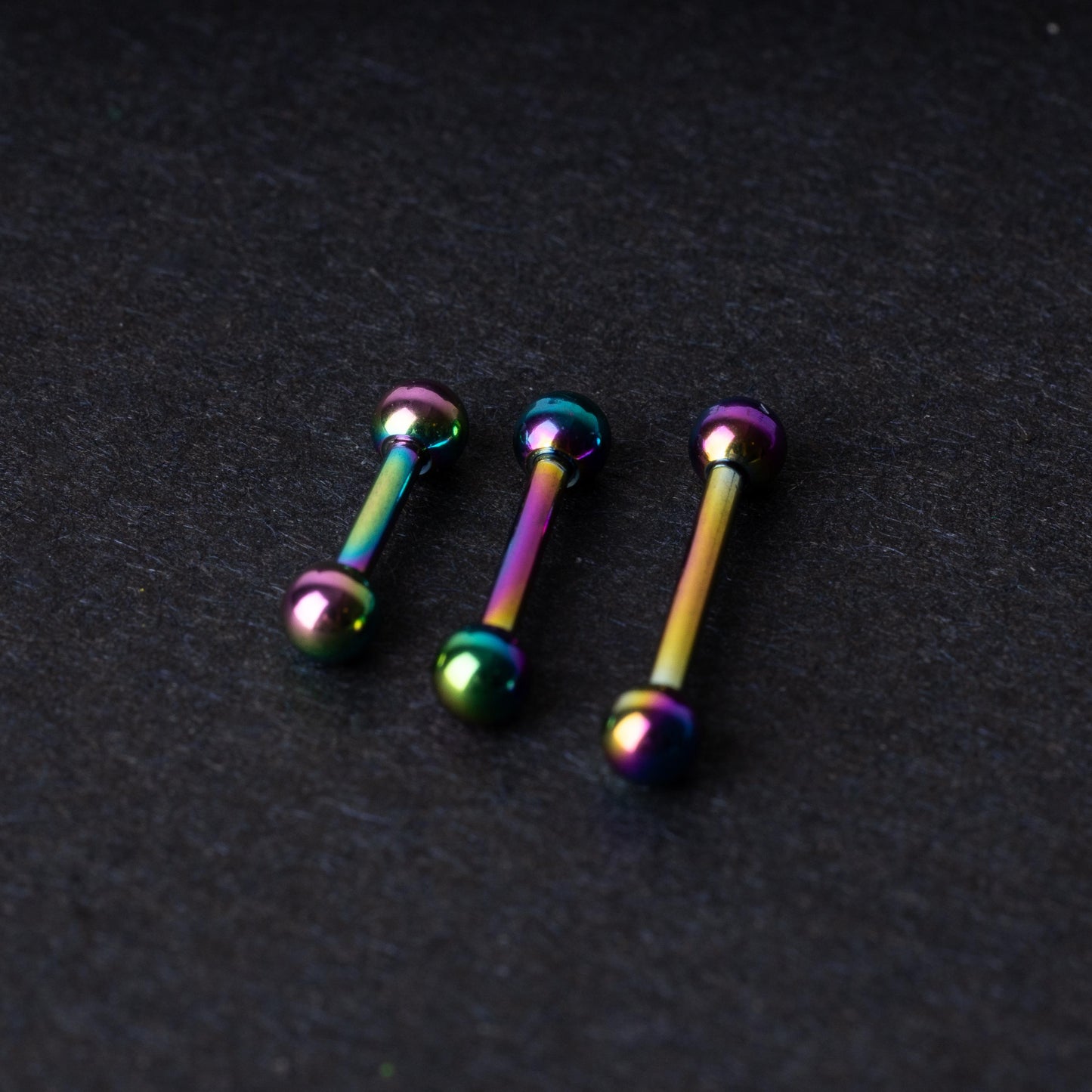 Rainbow stainless steel barbells with an anodized finish on a dark background.