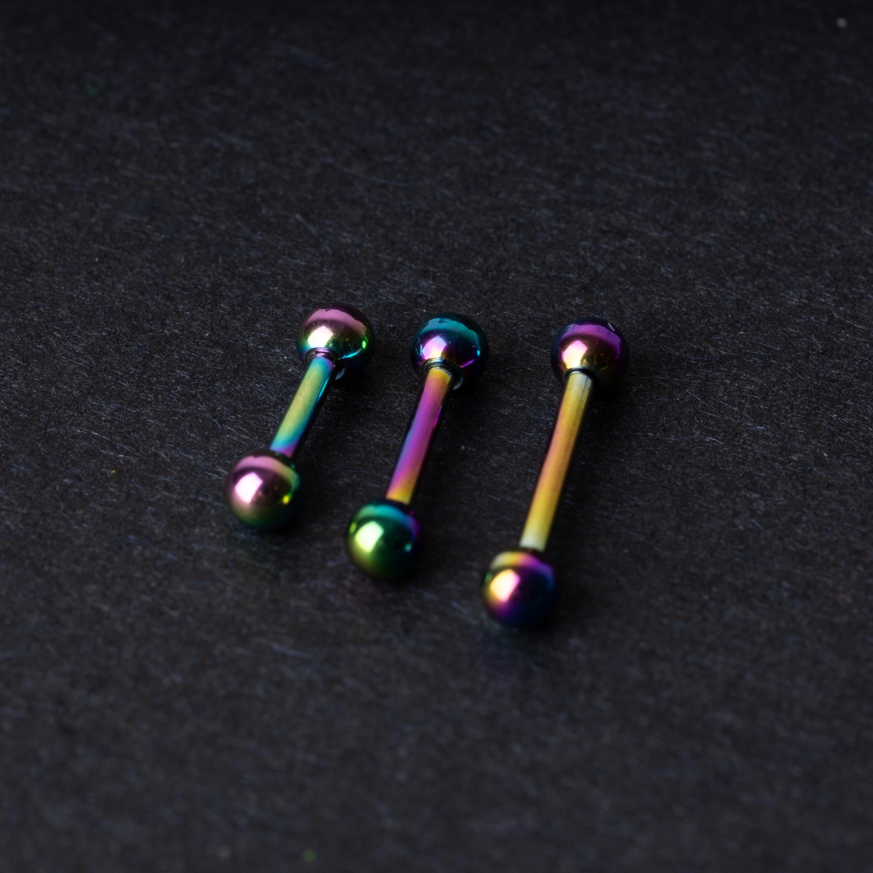 Rainbow stainless steel barbells with an anodized finish on a dark background.