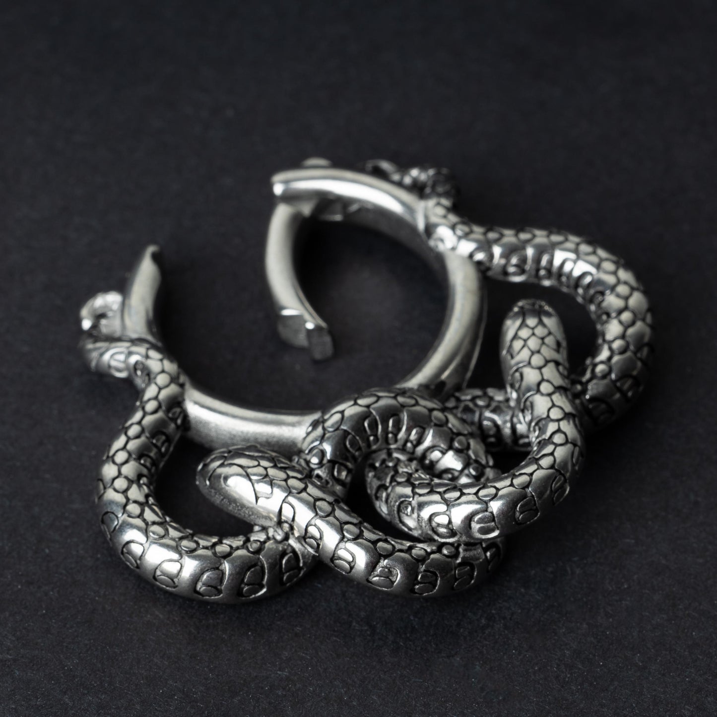 One open snake ear weight in polished silver, featuring detailed scales and a seamless hinge closure, displayed on a dark background.
