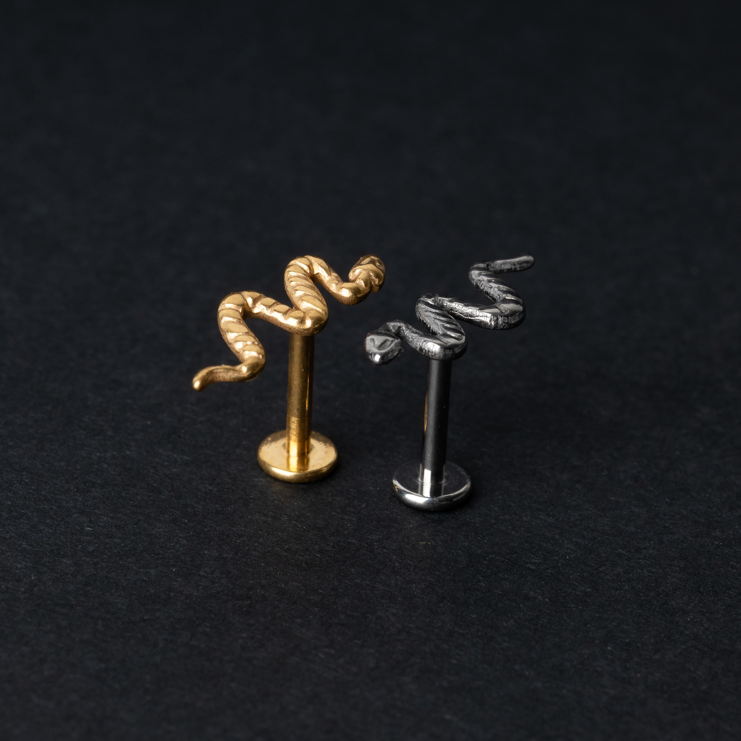 Gold-tone and silver-tone snake labret bars with intricate coiled snake designs displayed on a dark background.