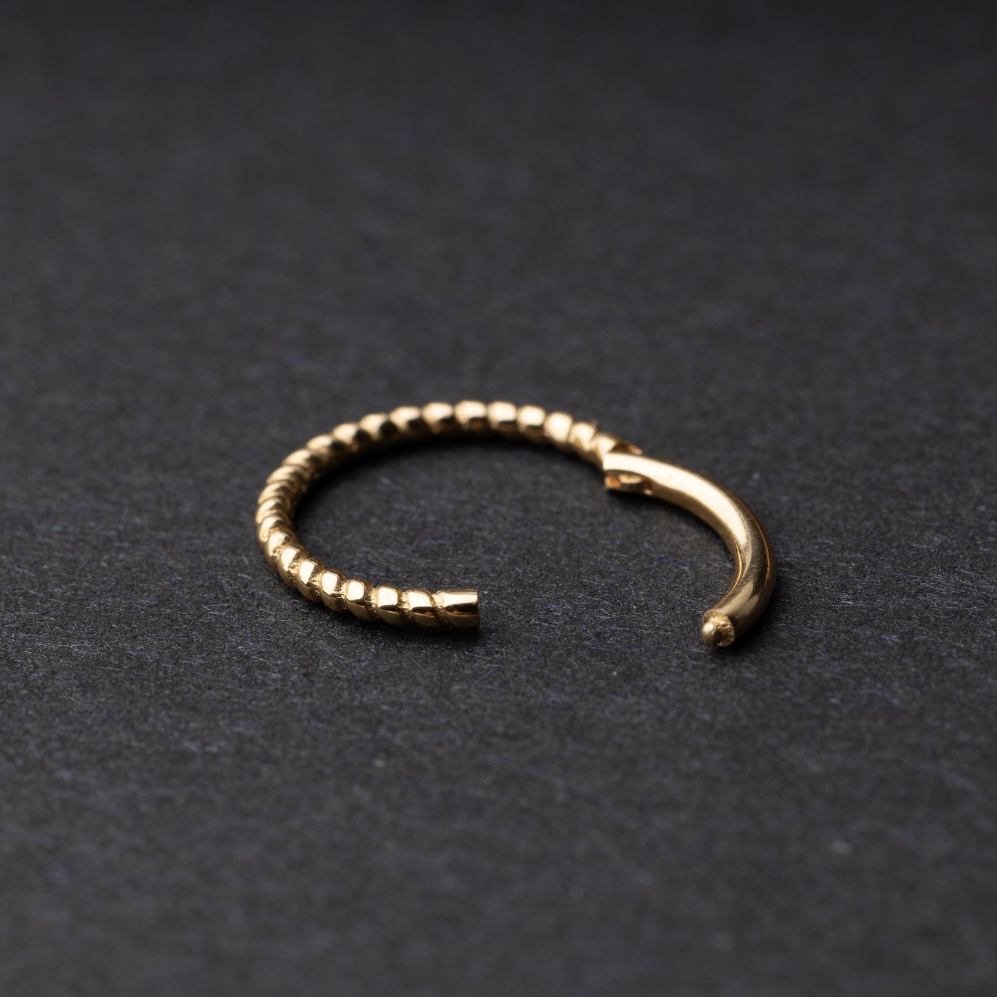 Close-up of a gold rope-textured septum clicker on a dark background, showcasing its intricate design and open hinge mechanism.