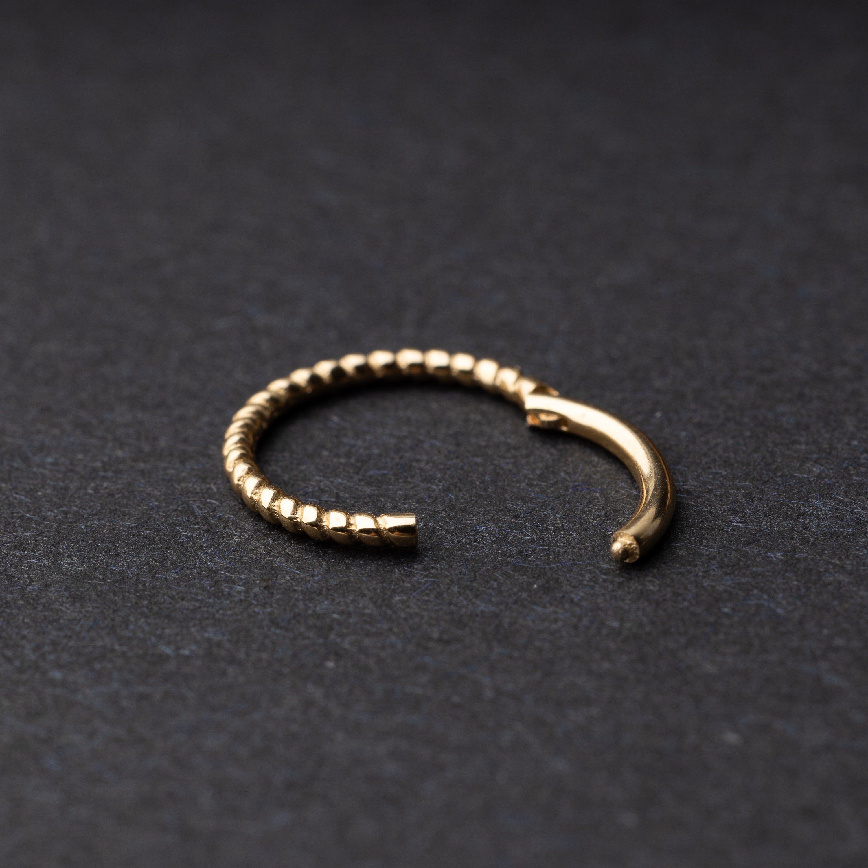 Close-up of a gold rope-textured septum clicker on a dark background, showcasing its intricate design and open hinge mechanism.