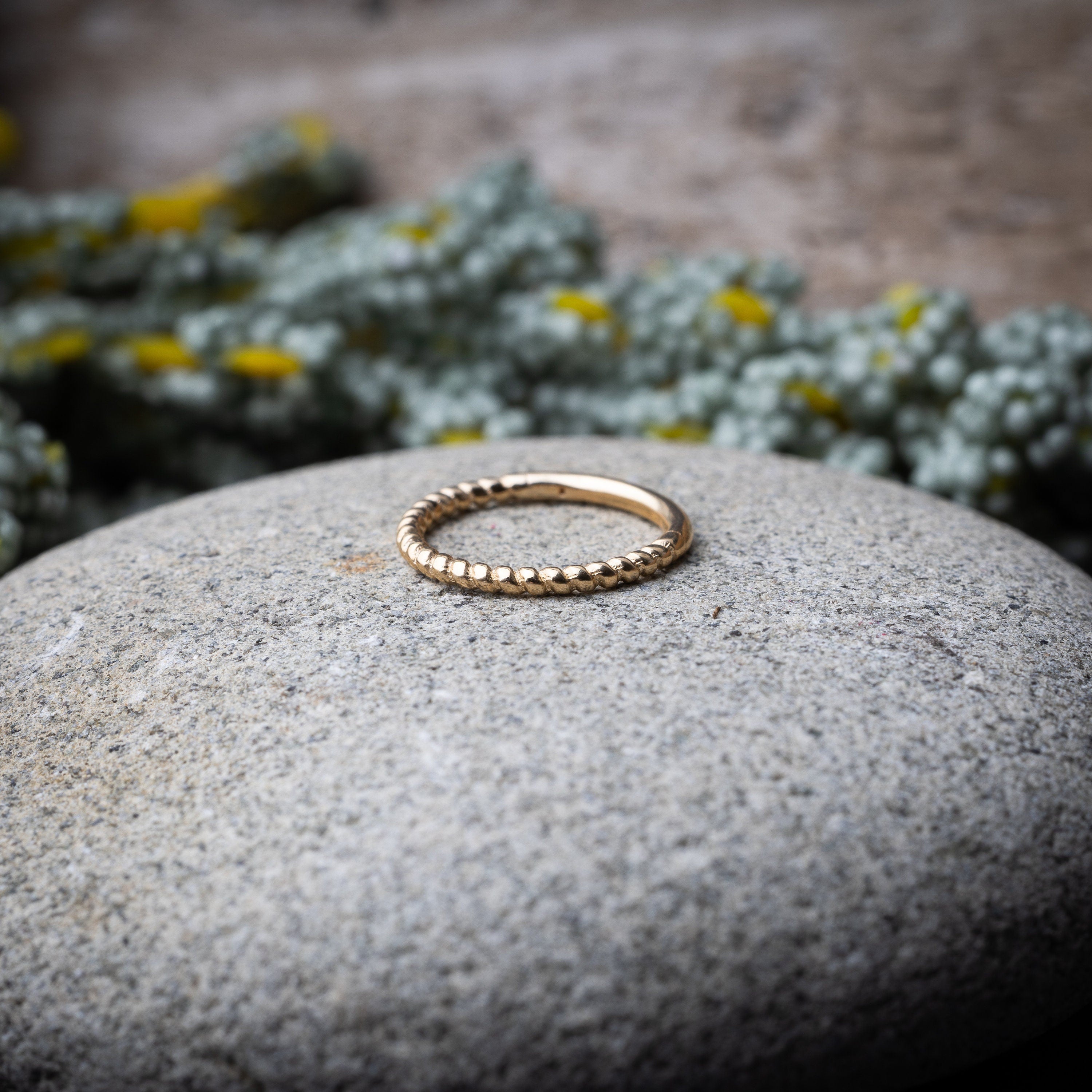 Close-up of a gold rope-textured septum clicker on a stone background, showcasing its intricate design and open hinge mechanism.