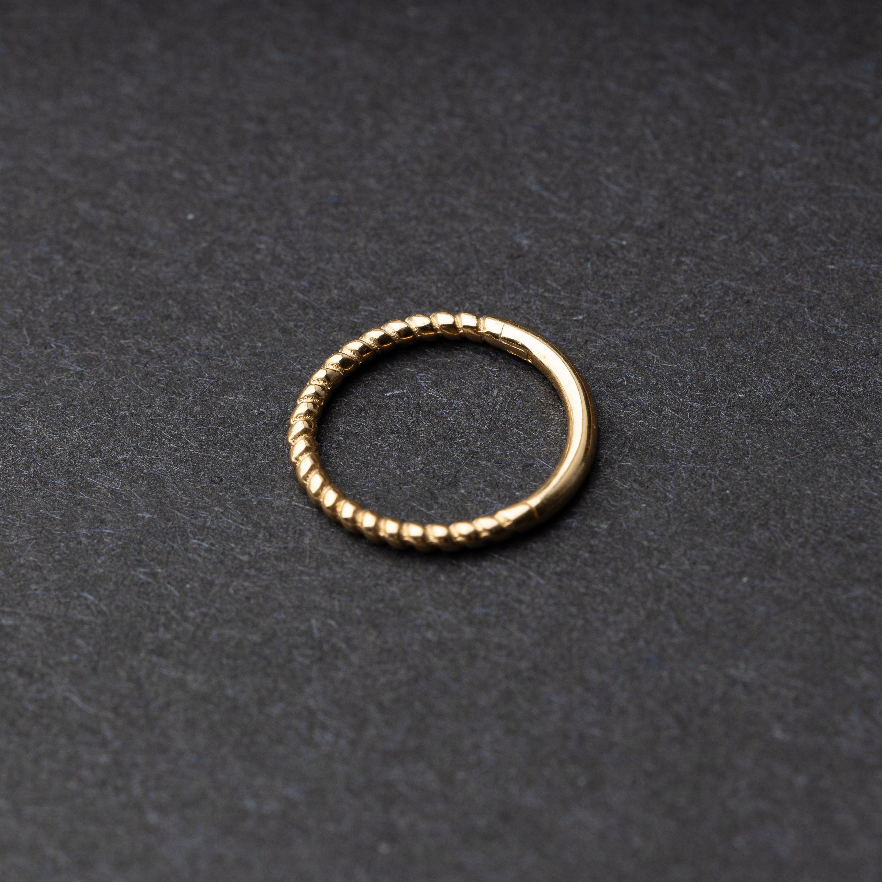 Close-up of a gold rope-textured septum clicker on a dark background, showcasing its intricate design and open hinge mechanism.