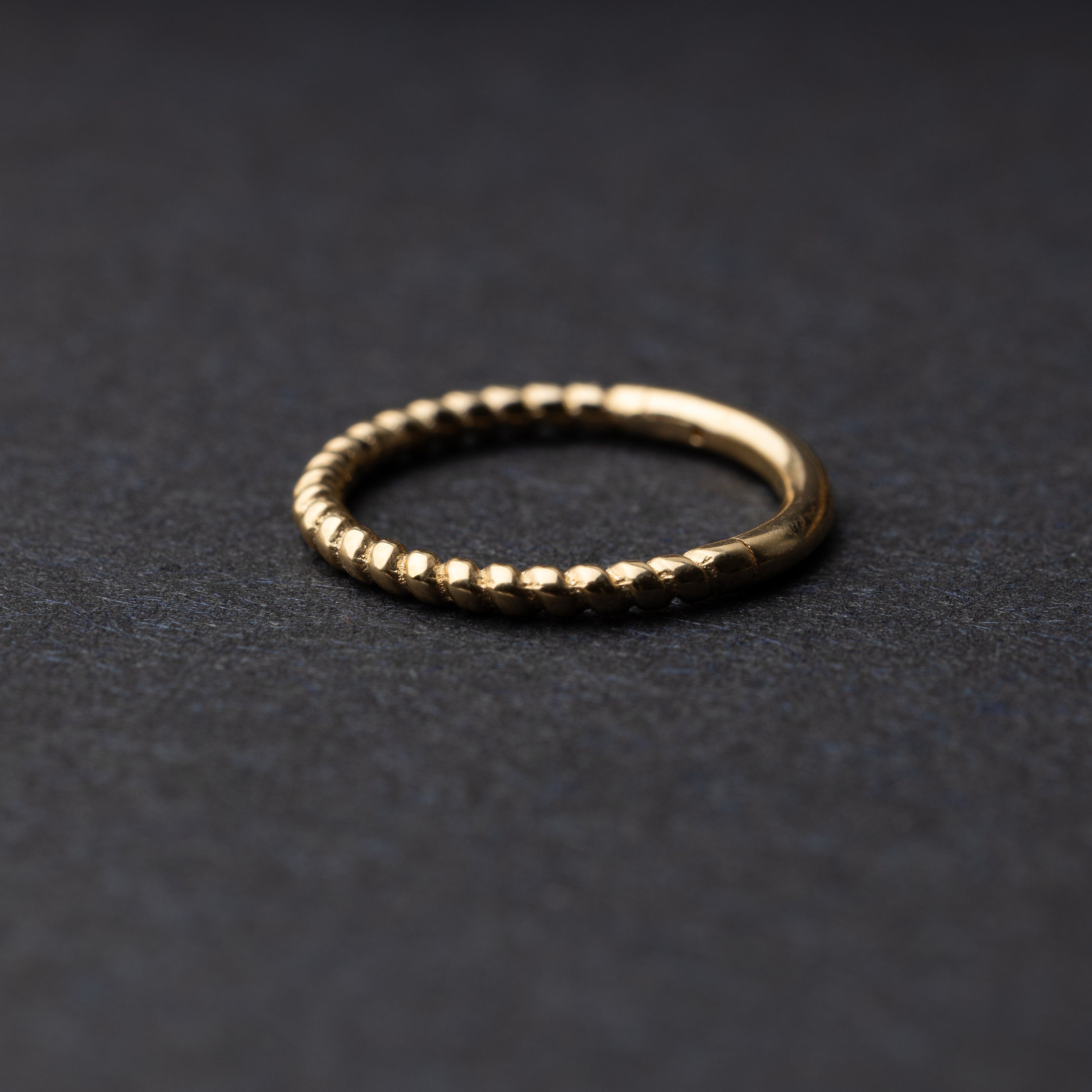 Close-up of a gold rope-textured septum clicker on a dark background, showcasing its intricate design and open hinge mechanism.