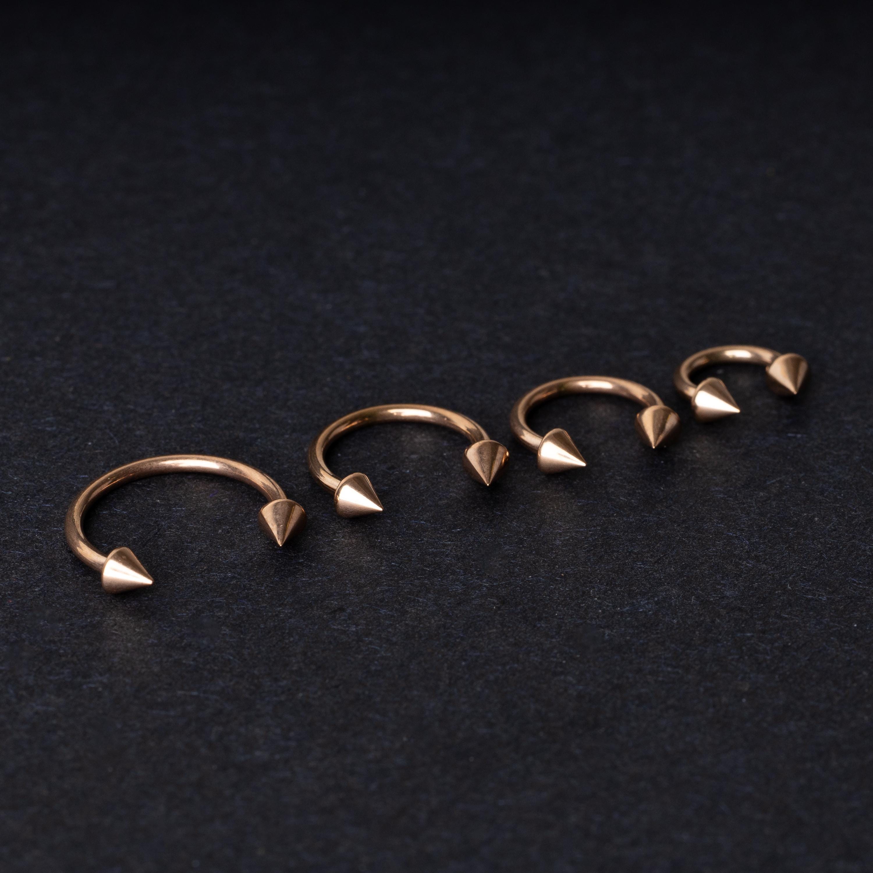 Four rose gold-tone horseshoe hoops with spike ends, arranged in descending size order on a dark textured background.
