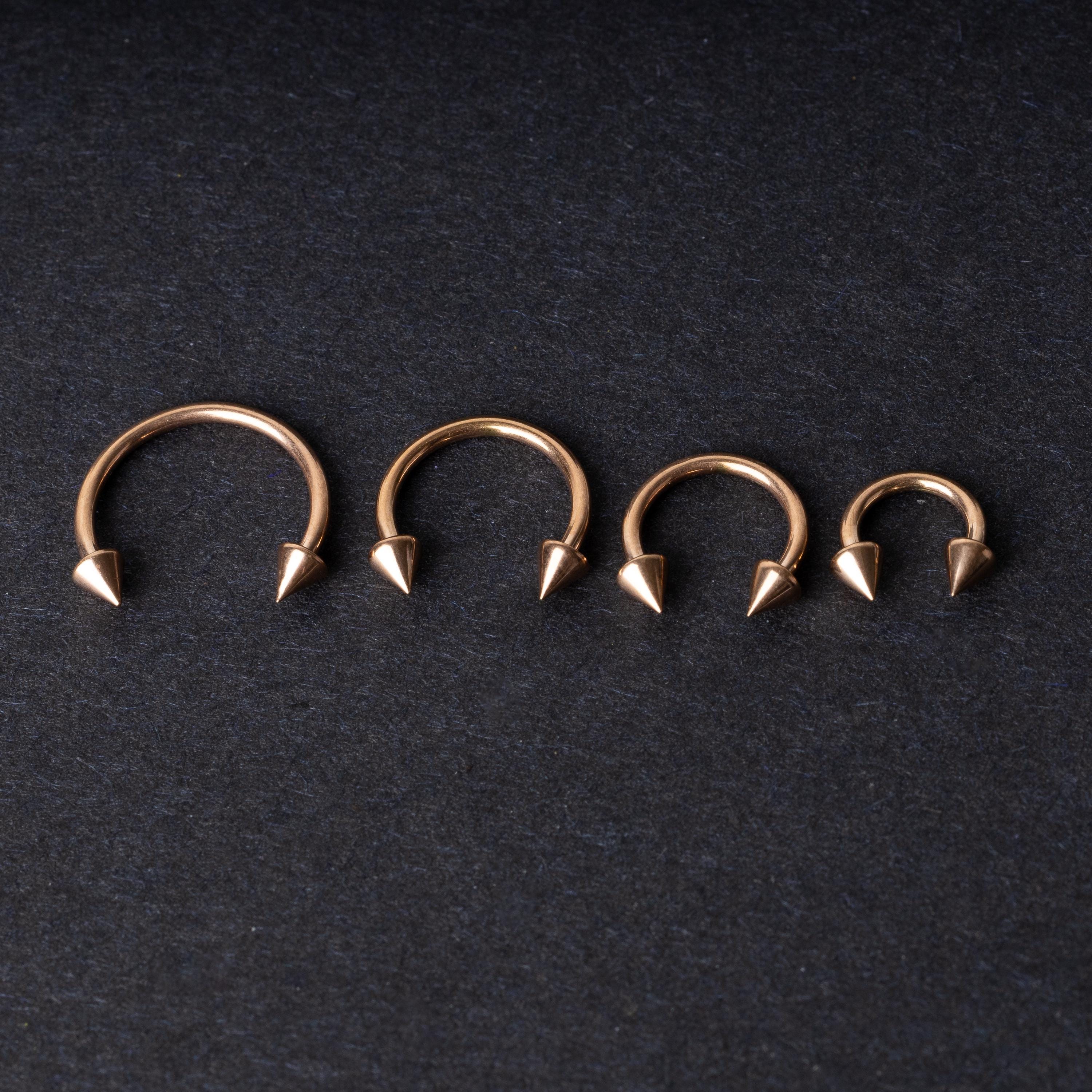 Four rose gold-tone horseshoe hoops with spike ends, arranged in descending size order on a dark textured background.