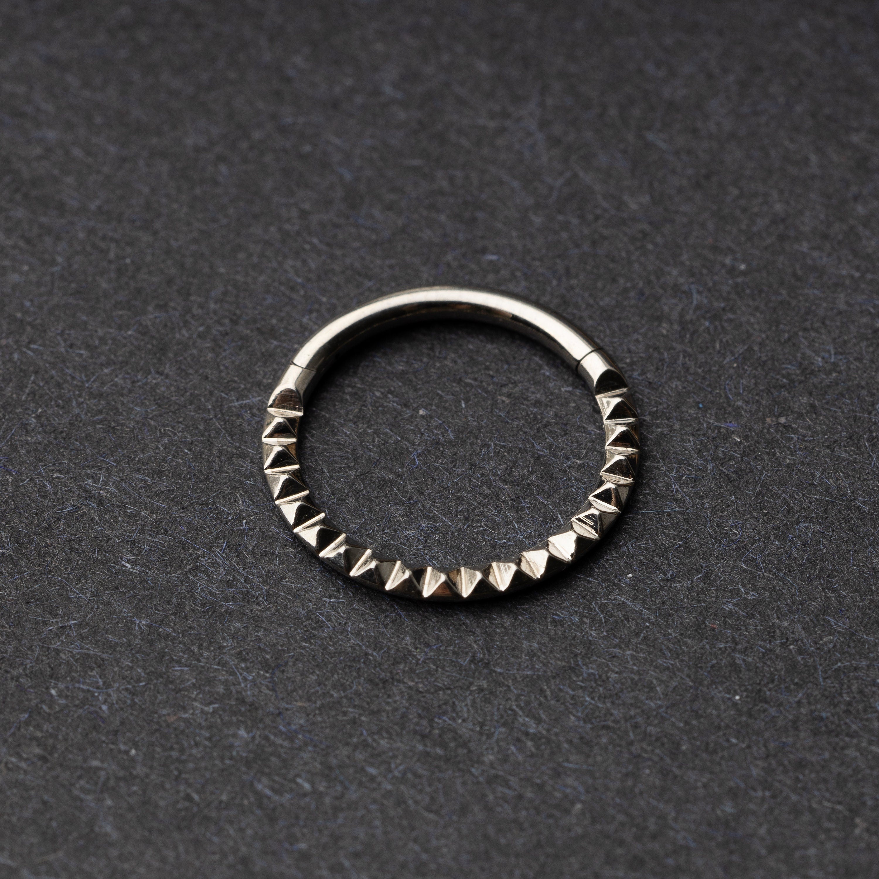 Spiked titanium clicker ring on a dark background.
