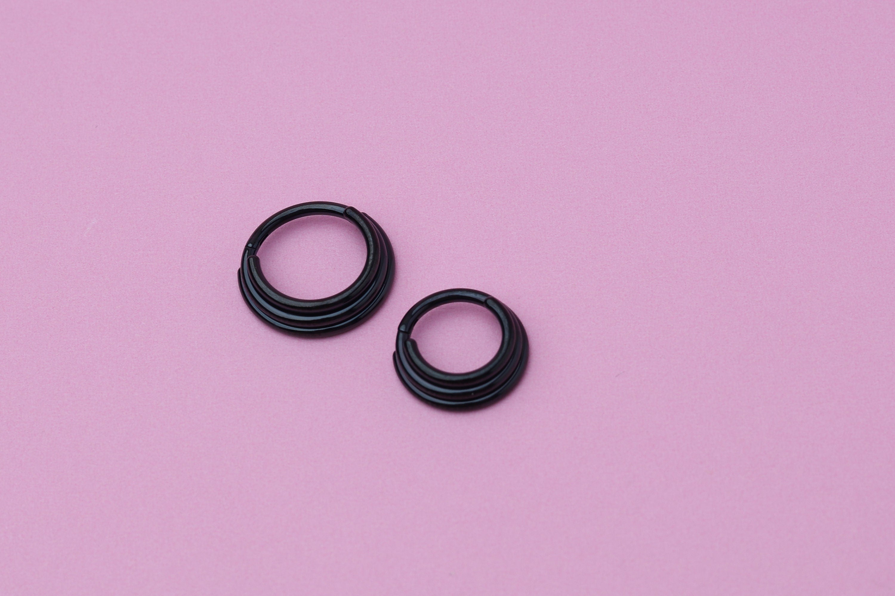Stacked Septum Clicker in black on a pink background.