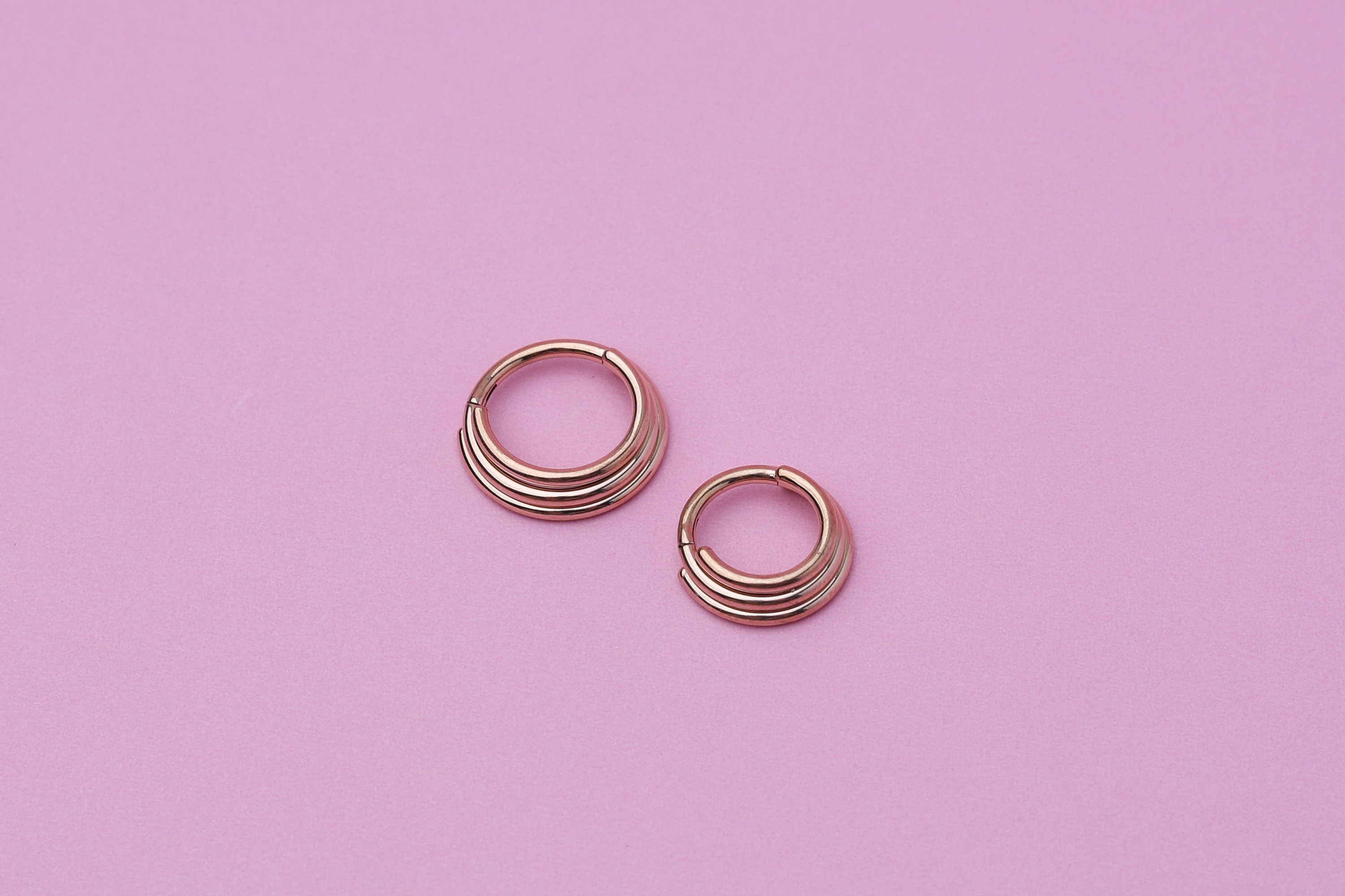 Stacked Septum Clicker in rose gold on a pink background.