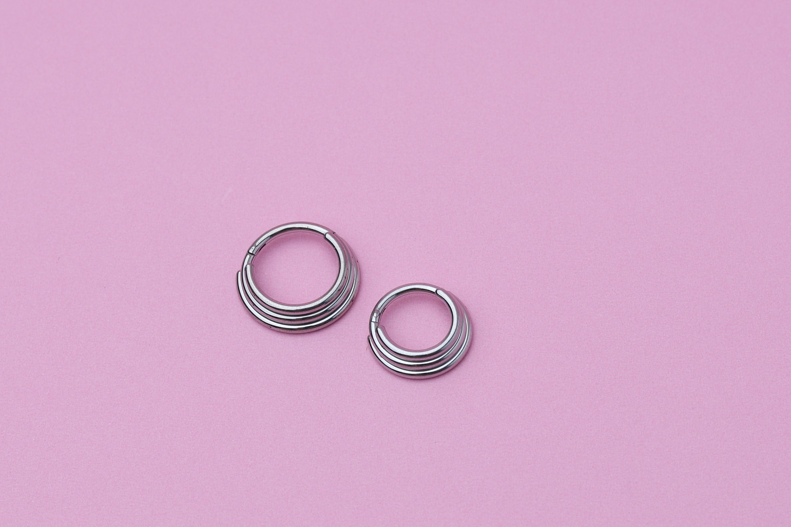 Stacked Septum Clicker in silver on a pink background.