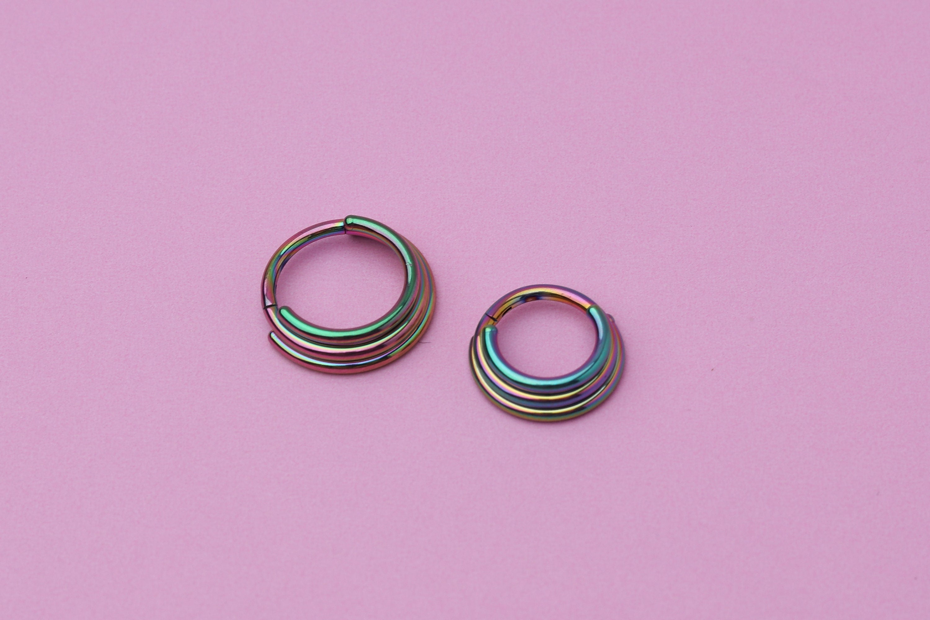 Stacked Septum Clicker in rainbow on a pink background.