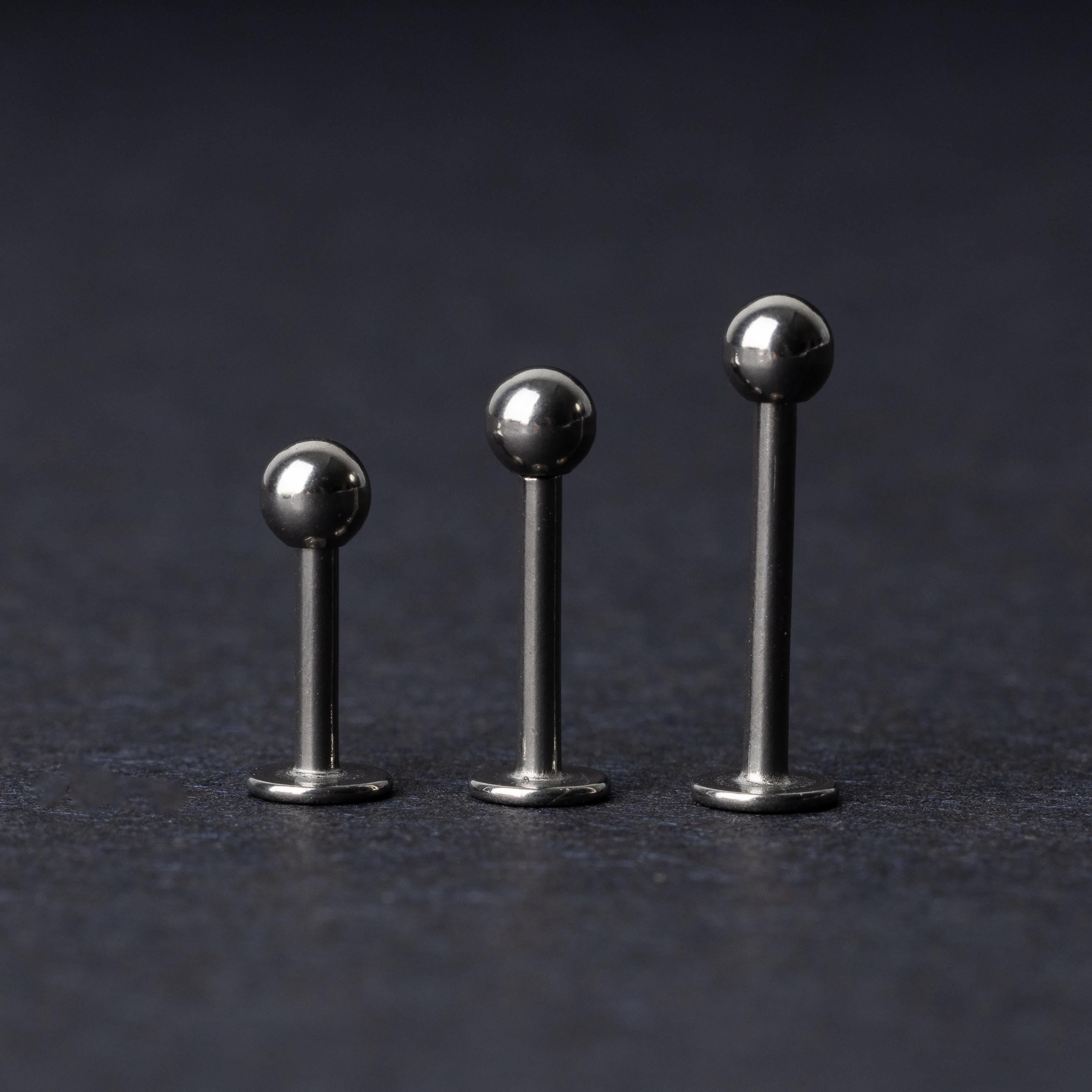 Three silver stainless steel labret studs with flat backs and polished ball ends, displayed on a dark textured background.