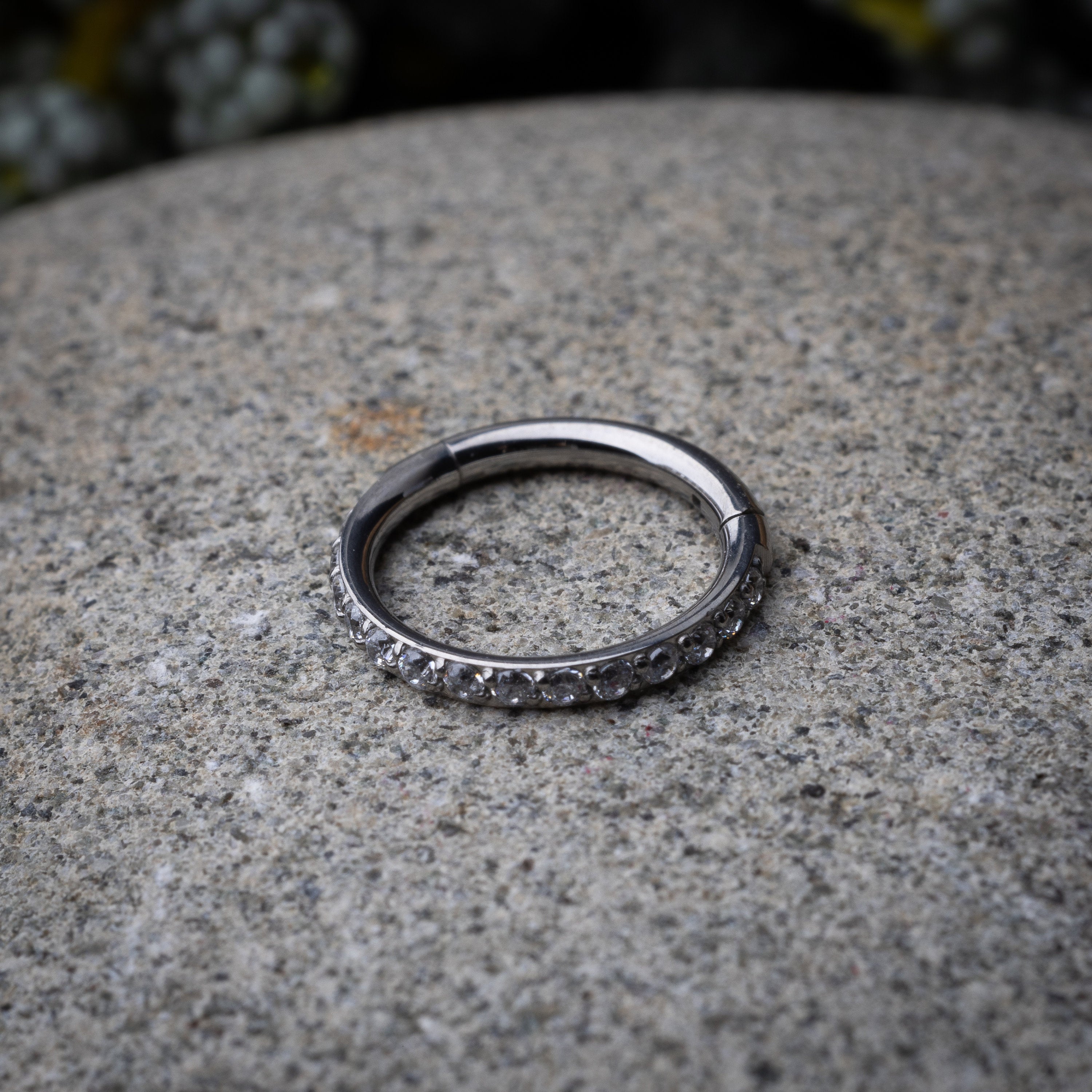 A stainless steel hoop with a row of clear sparkling gems displayed on a stone background.