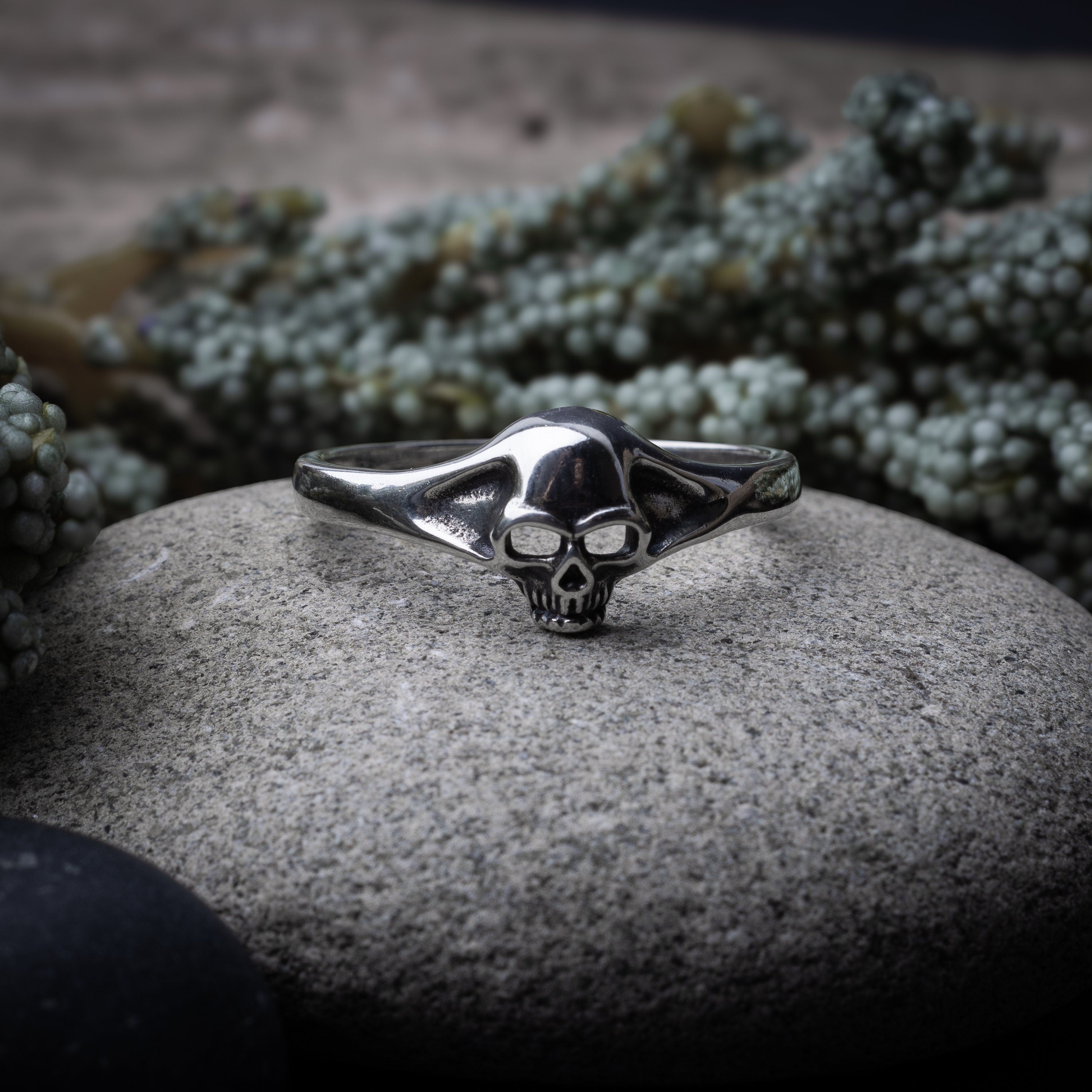 Sterling silver ring featuring a detailed skull design, displayed on a stone background.
