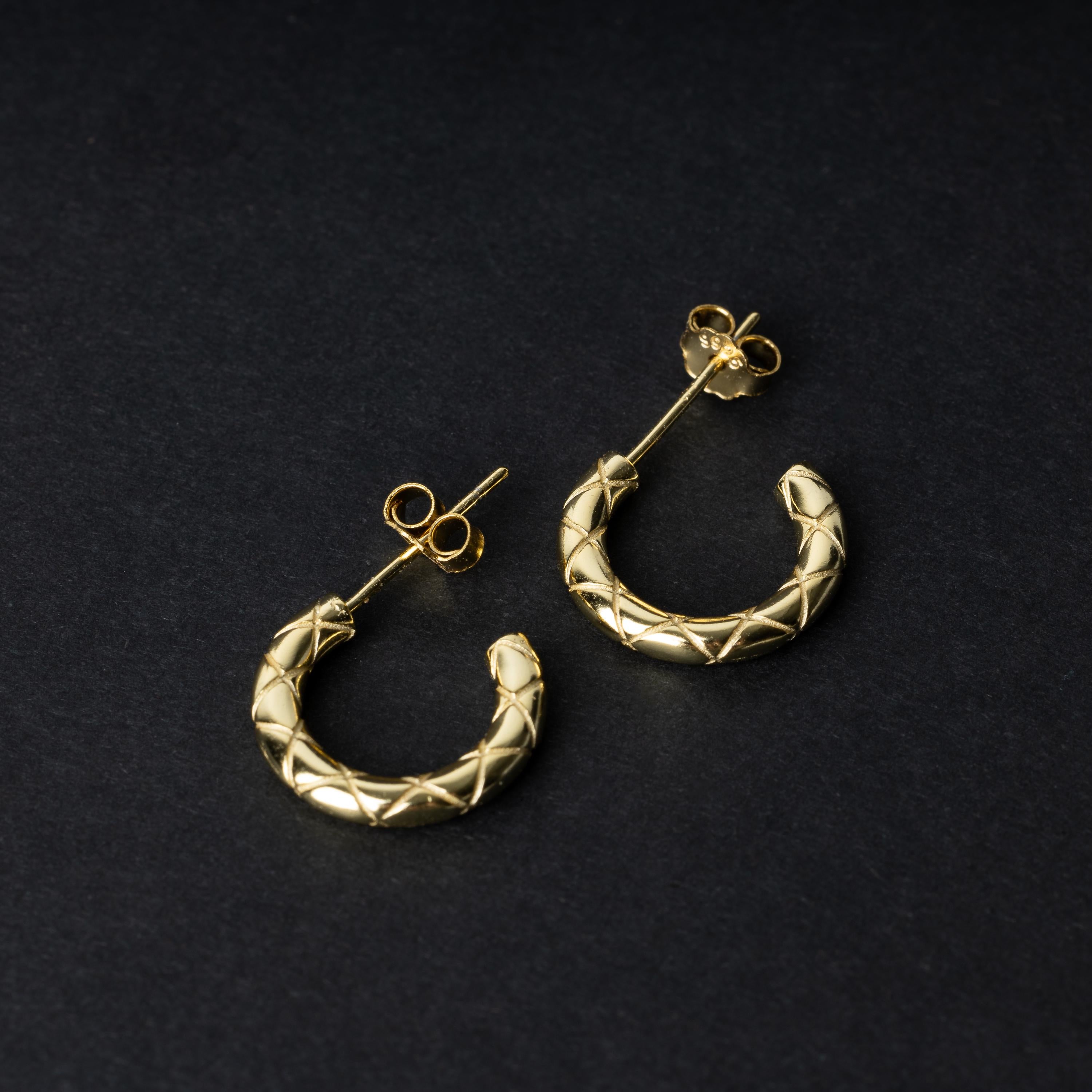 A pair of small gold quilted hoop earrings with post backs displayed on a dark background.