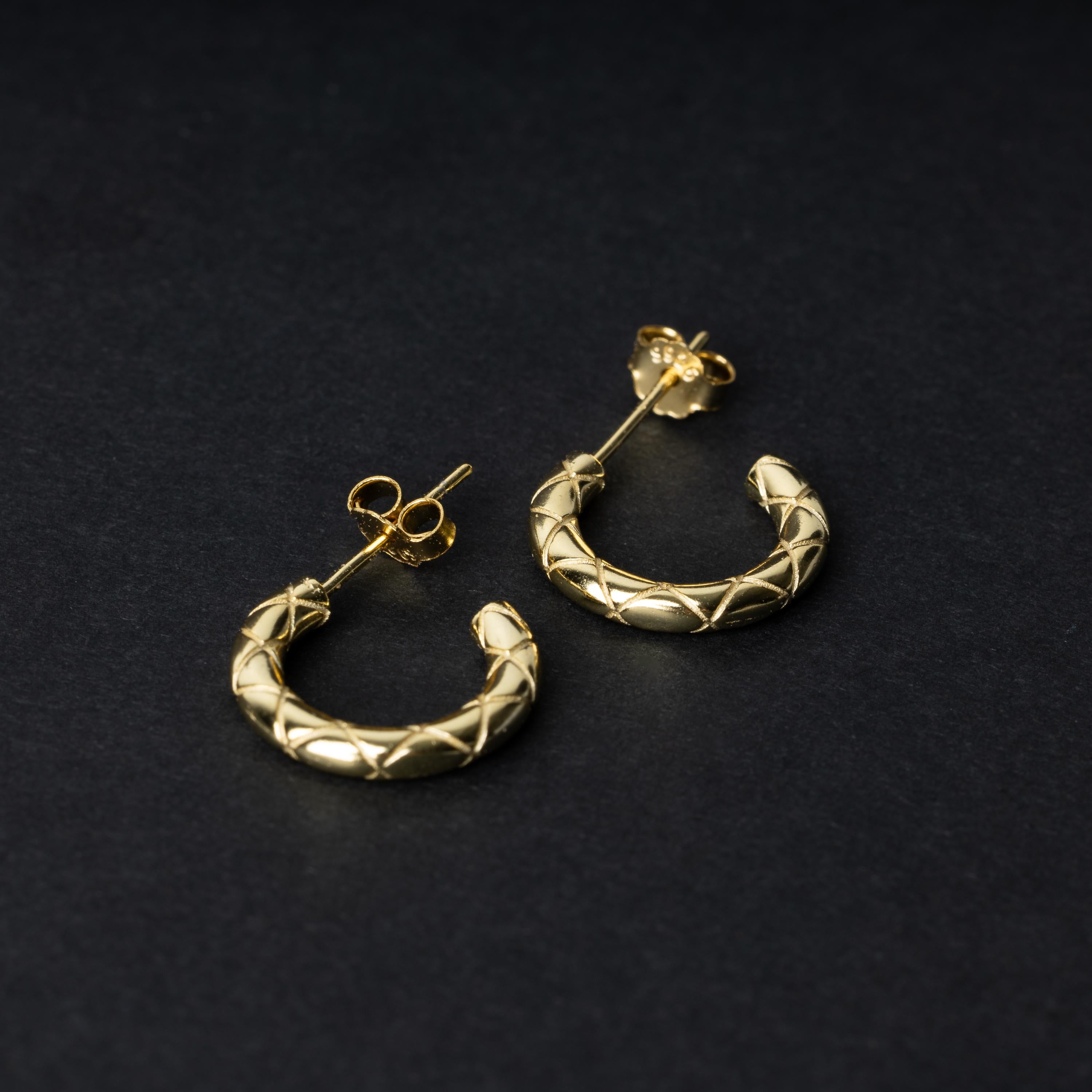 A pair of small gold quilted hoop earrings with post backs displayed on a dark background.