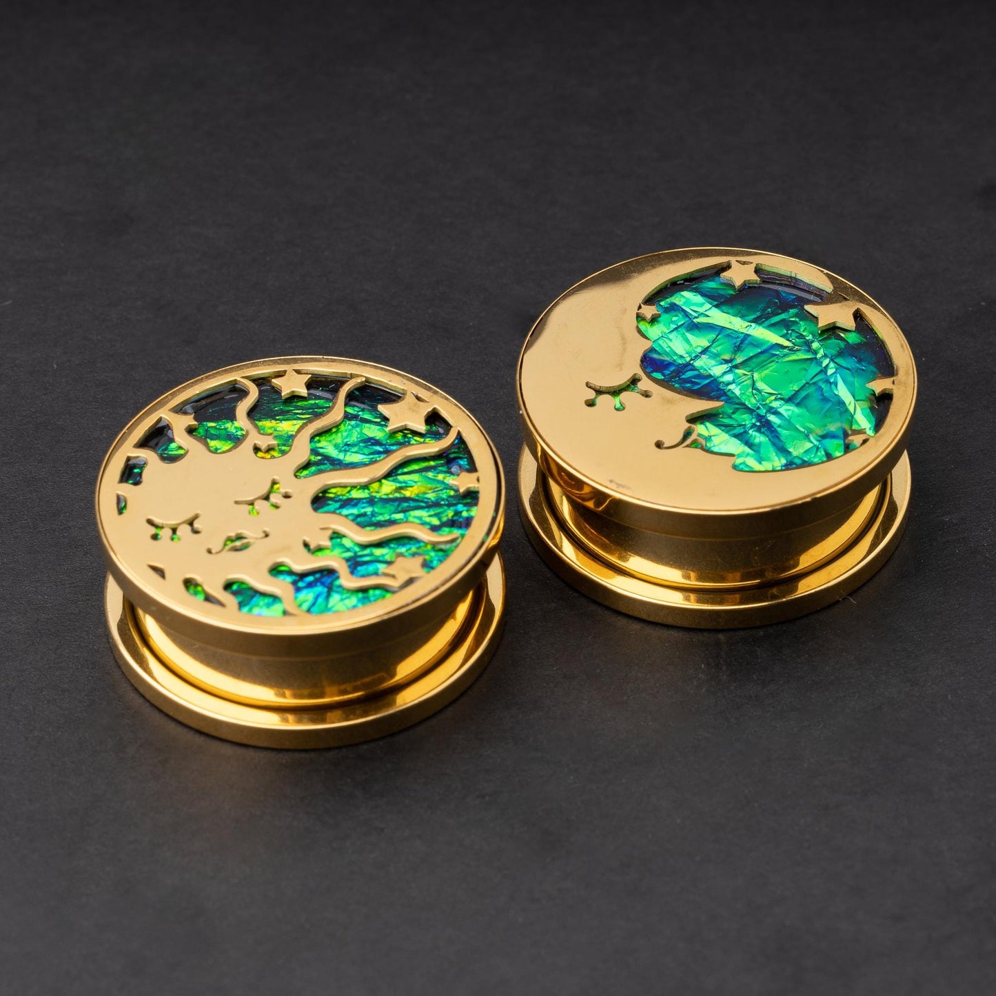 Gold plugs with sun and moon designs, accented by iridescent abalone inlay, displayed on a dark background.