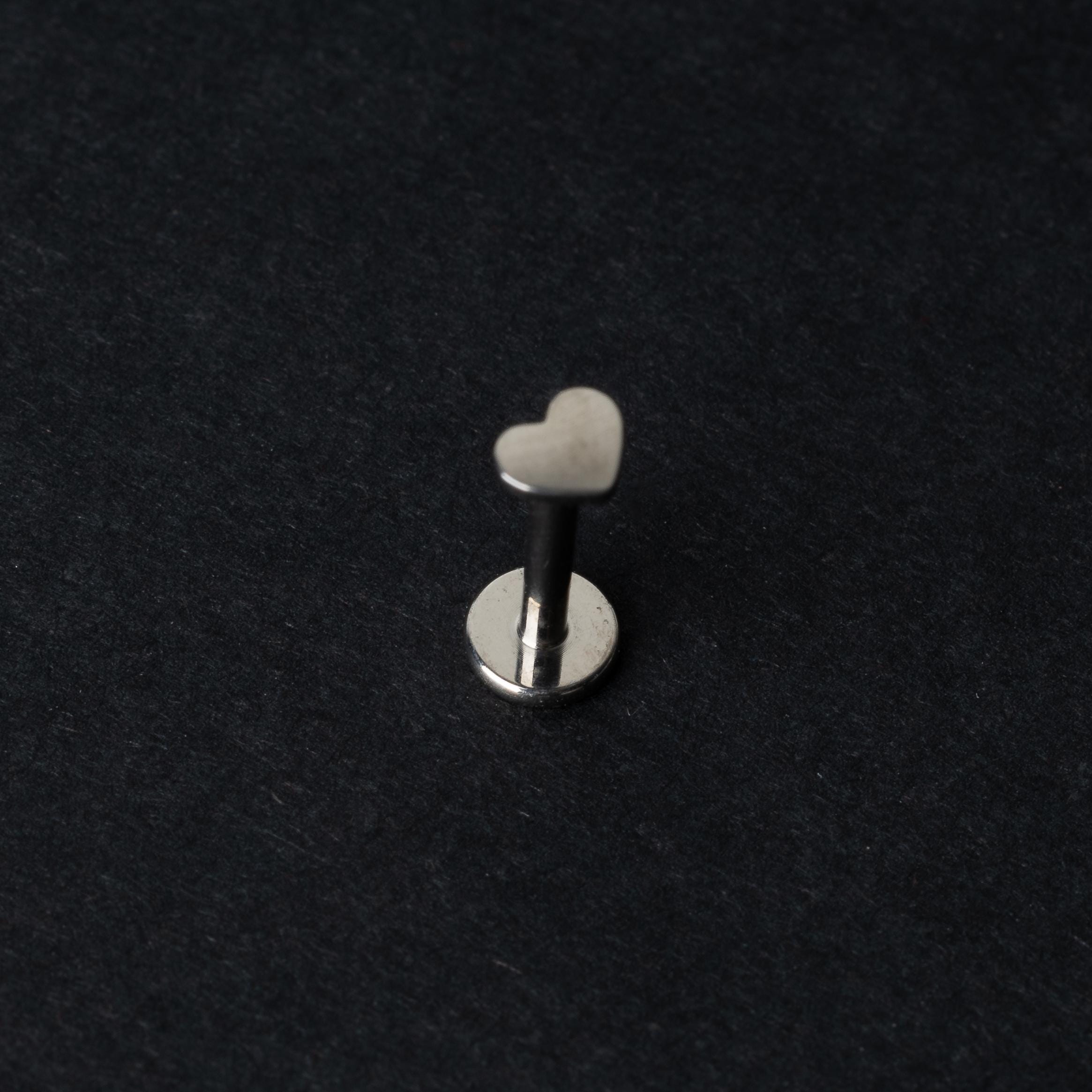 Heart-shaped titanium labret stud on a dark background.