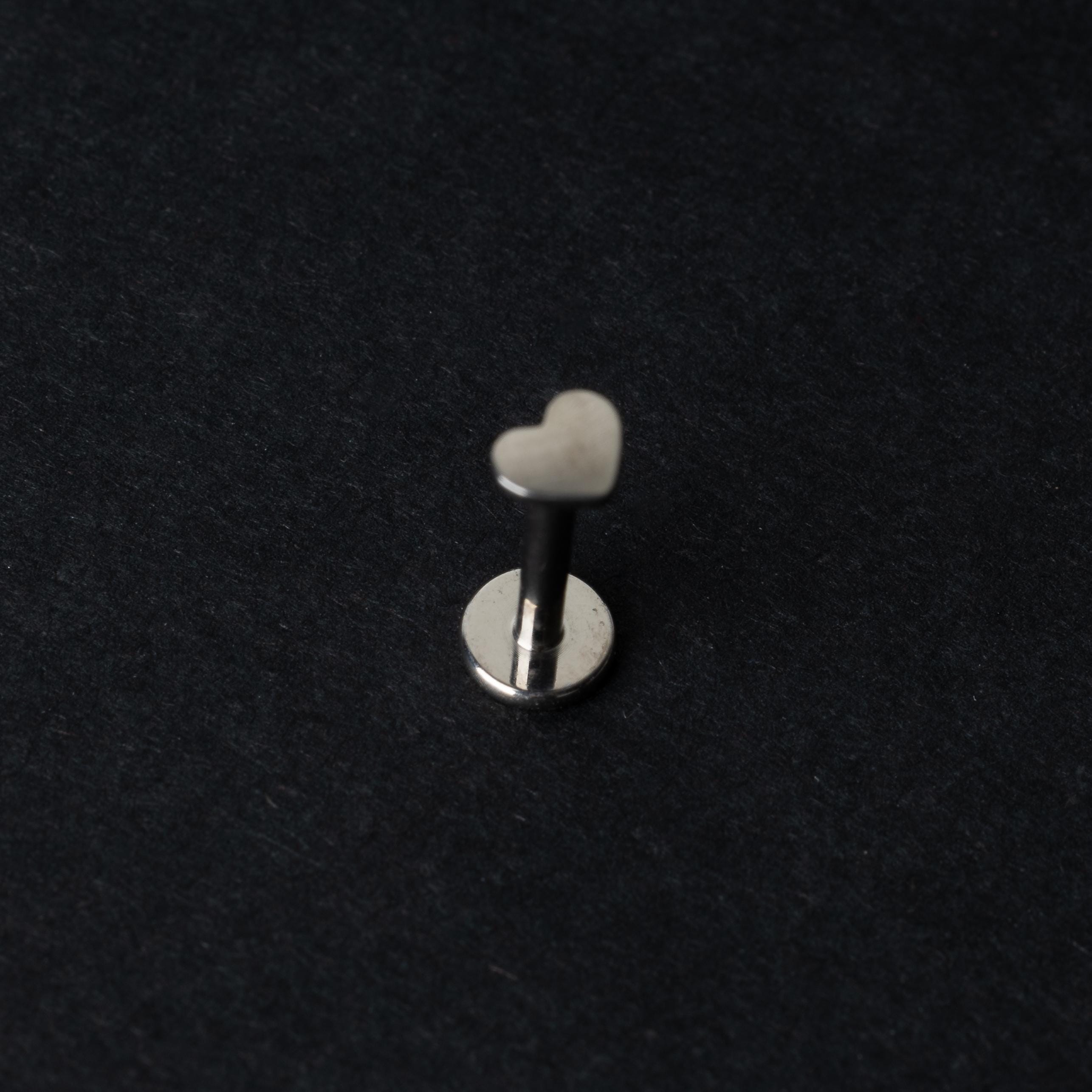 Heart-shaped titanium labret stud on a dark background.