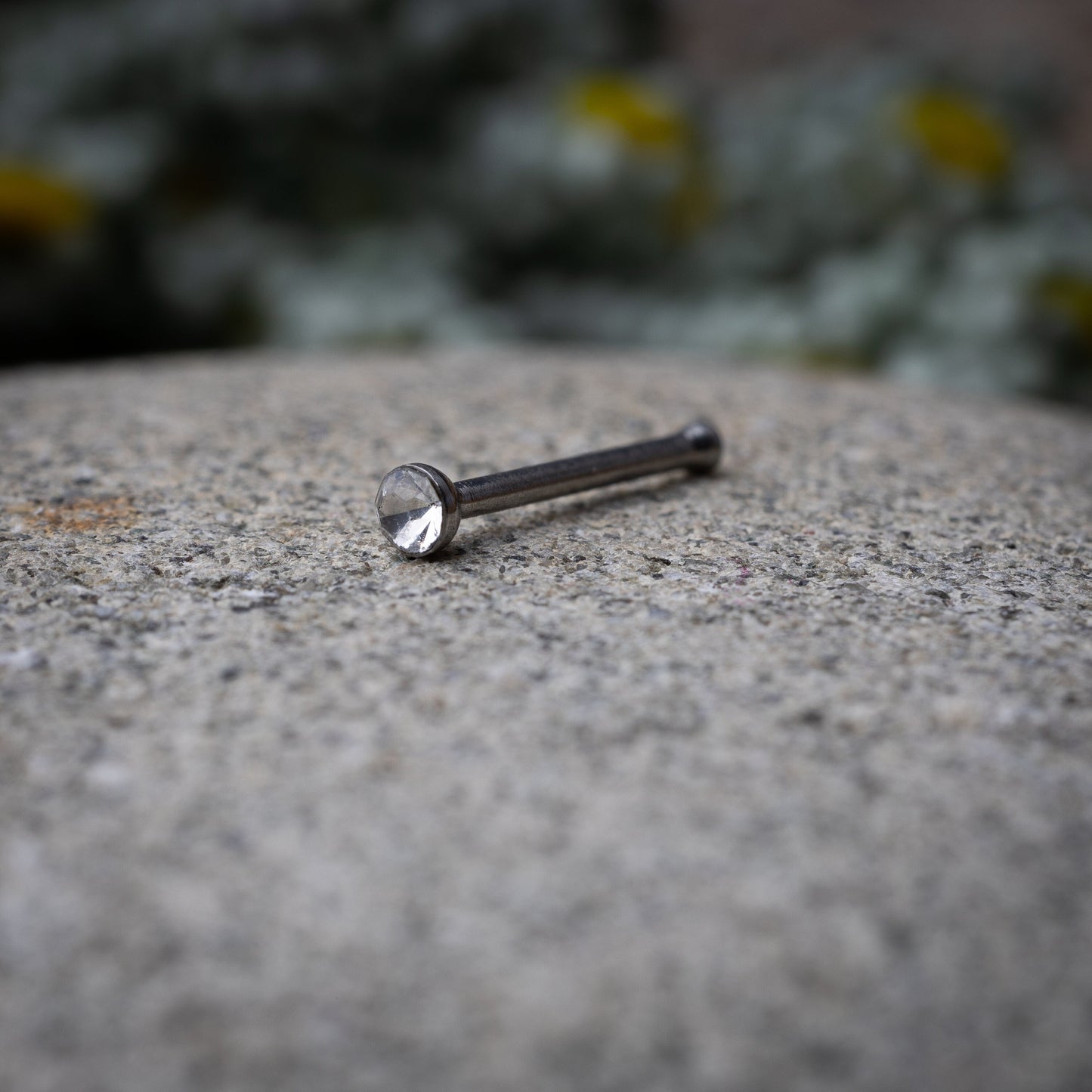 Stainless steel nose stud with a small crystal accent, displayed on a dark textured background.