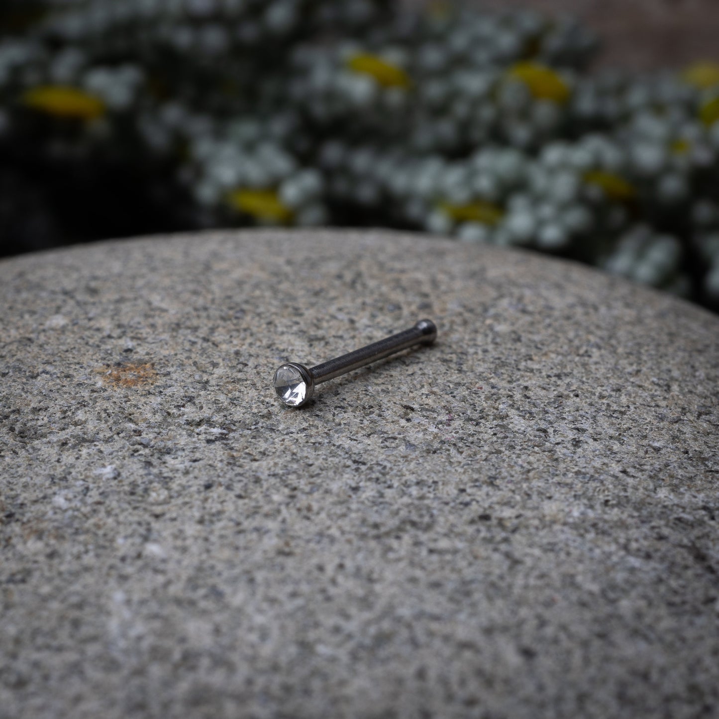 Stainless steel nose stud with a small crystal accent, displayed on a dark textured background.