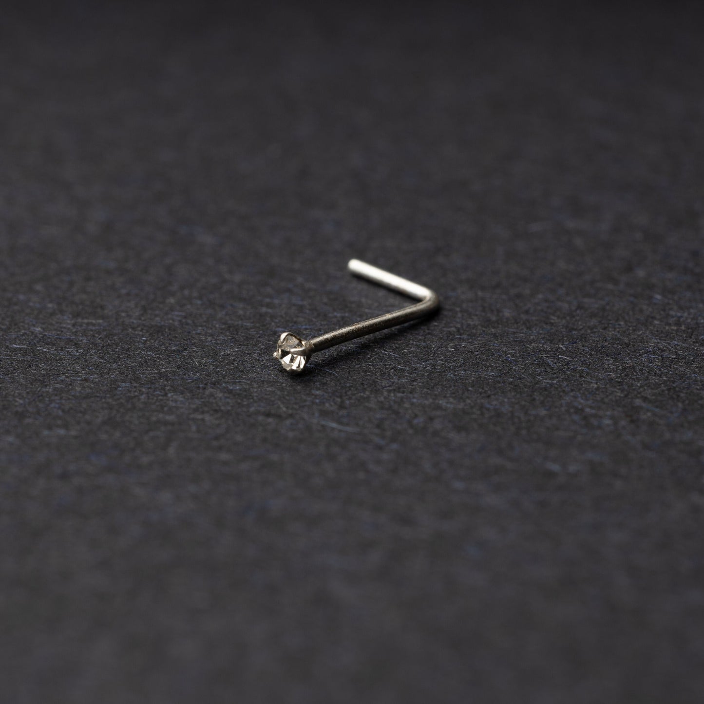 925 sterling silver nose stud with a small crystal accent, displayed on a dark textured background.