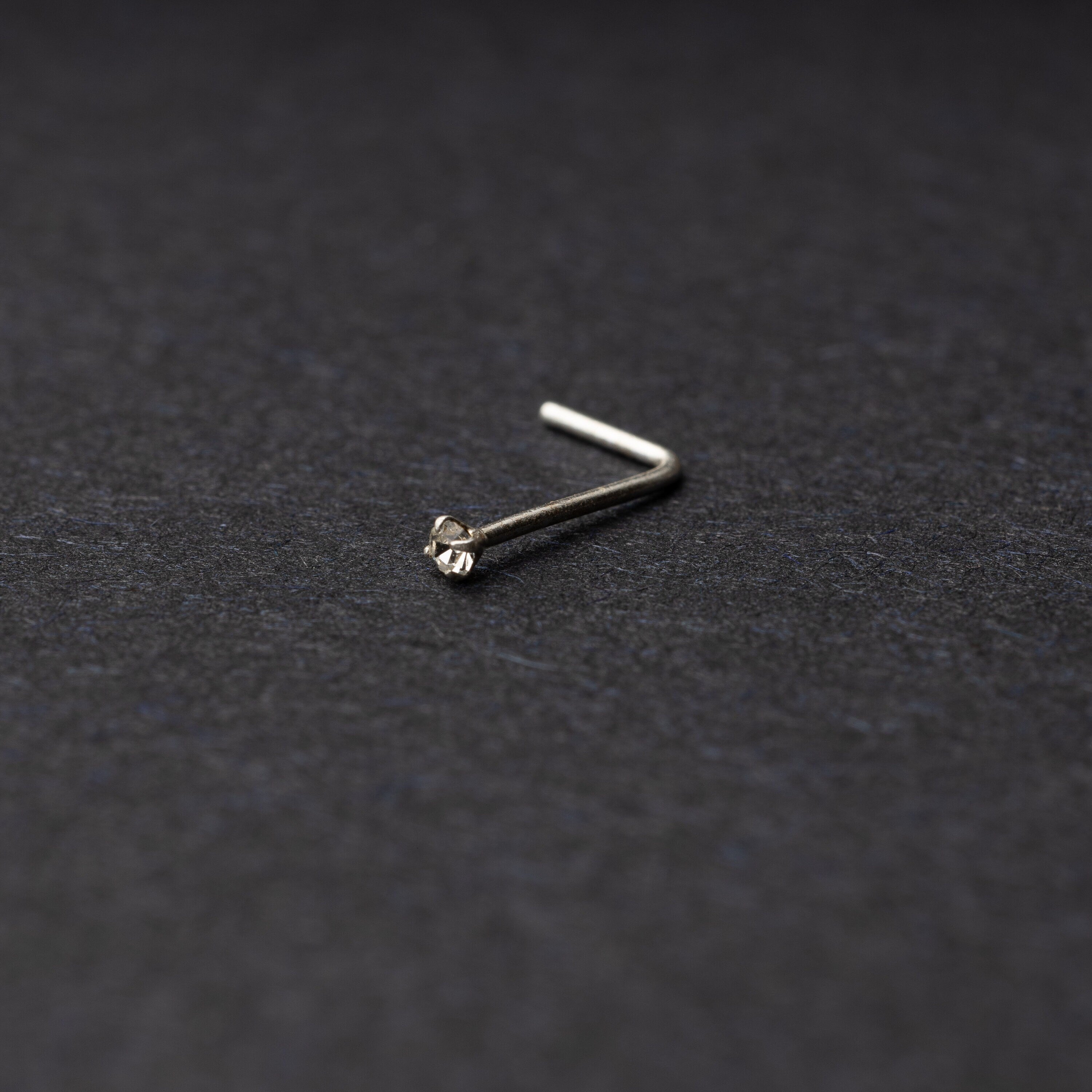 925 sterling silver nose stud with a small crystal accent, displayed on a dark textured background.