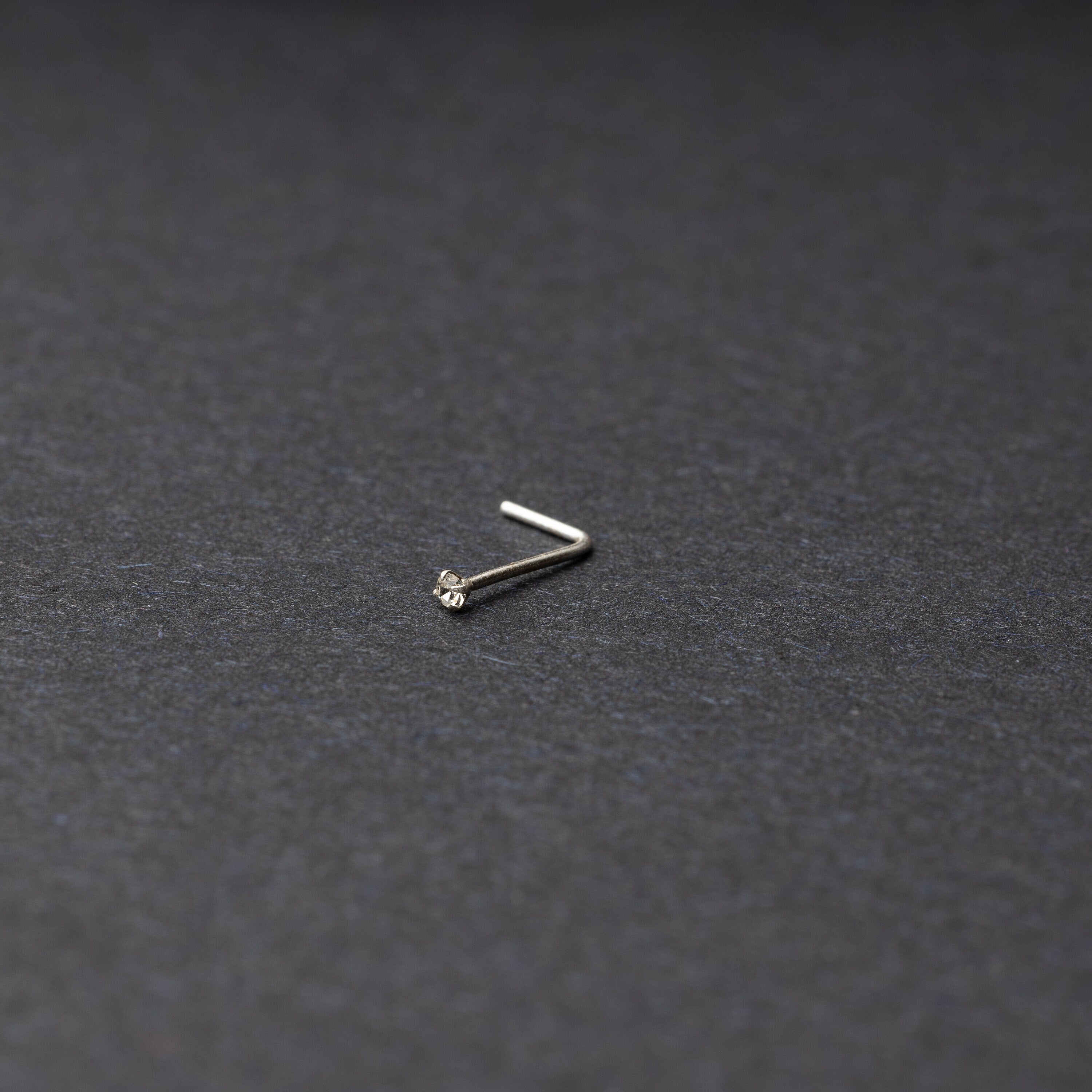 925 sterling silver nose stud with a small crystal accent, displayed on a dark textured background.
