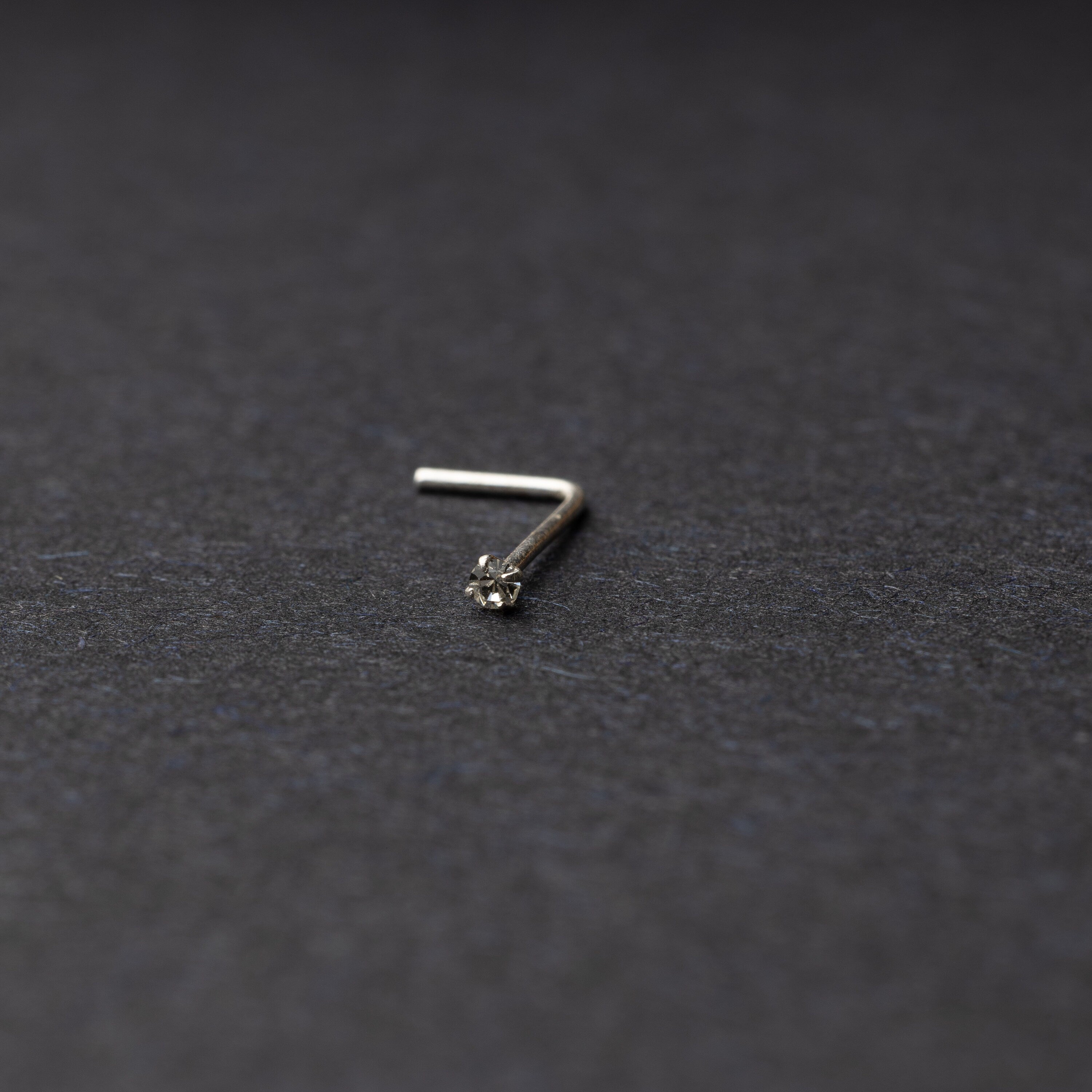 925 sterling silver nose stud with a small crystal accent, displayed on a dark textured background.