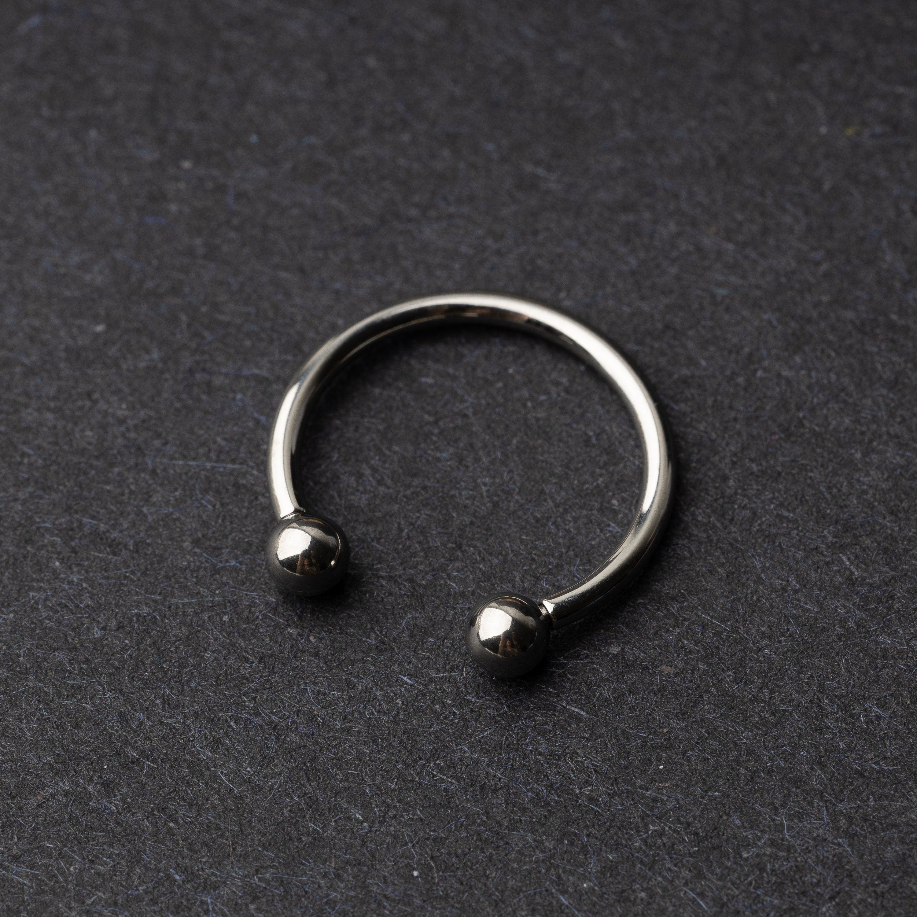 Titanium horseshoe ring with ball ends, displayed on a dark textured background.