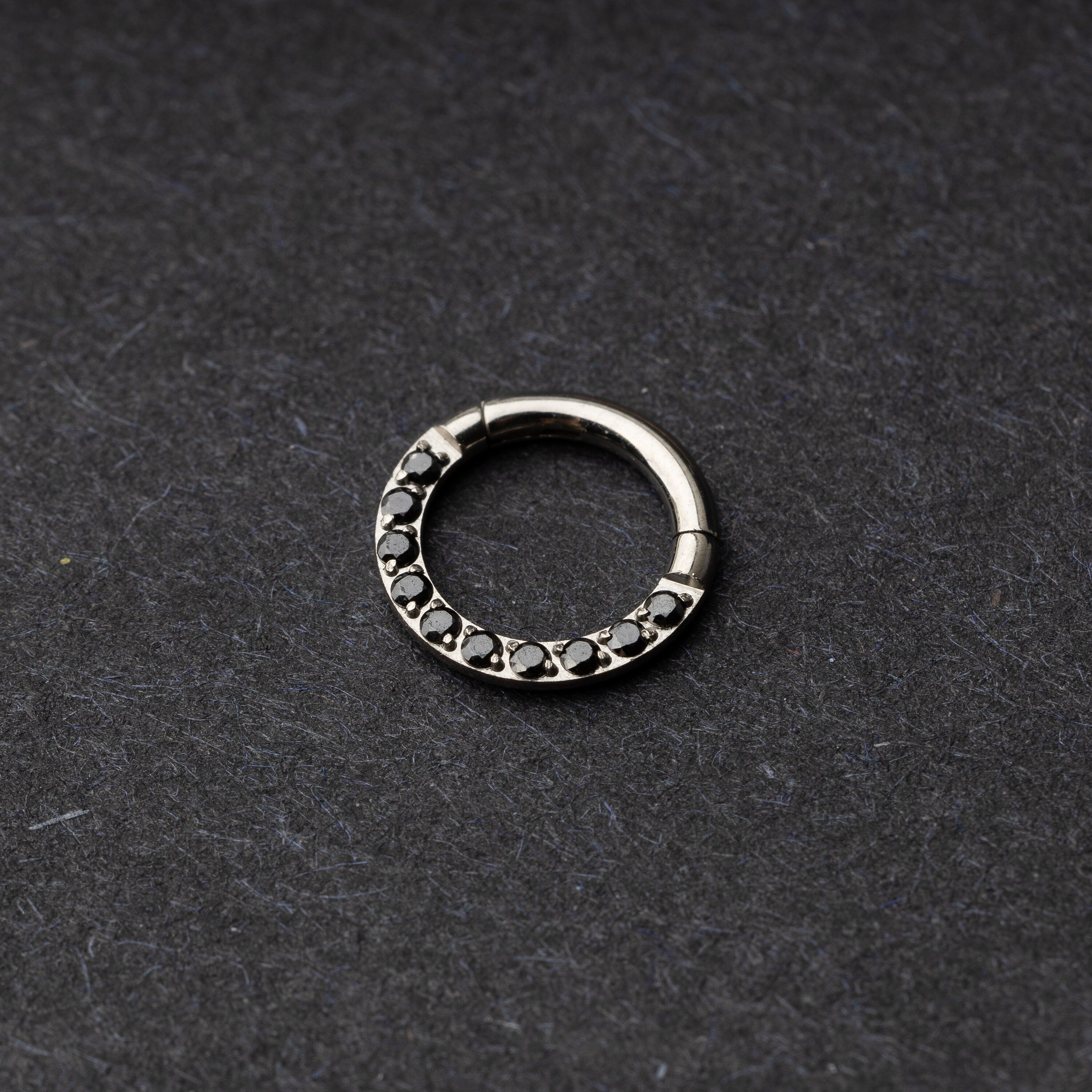 Titanium septum clicker with black gemstones, displayed on a textured dark background.