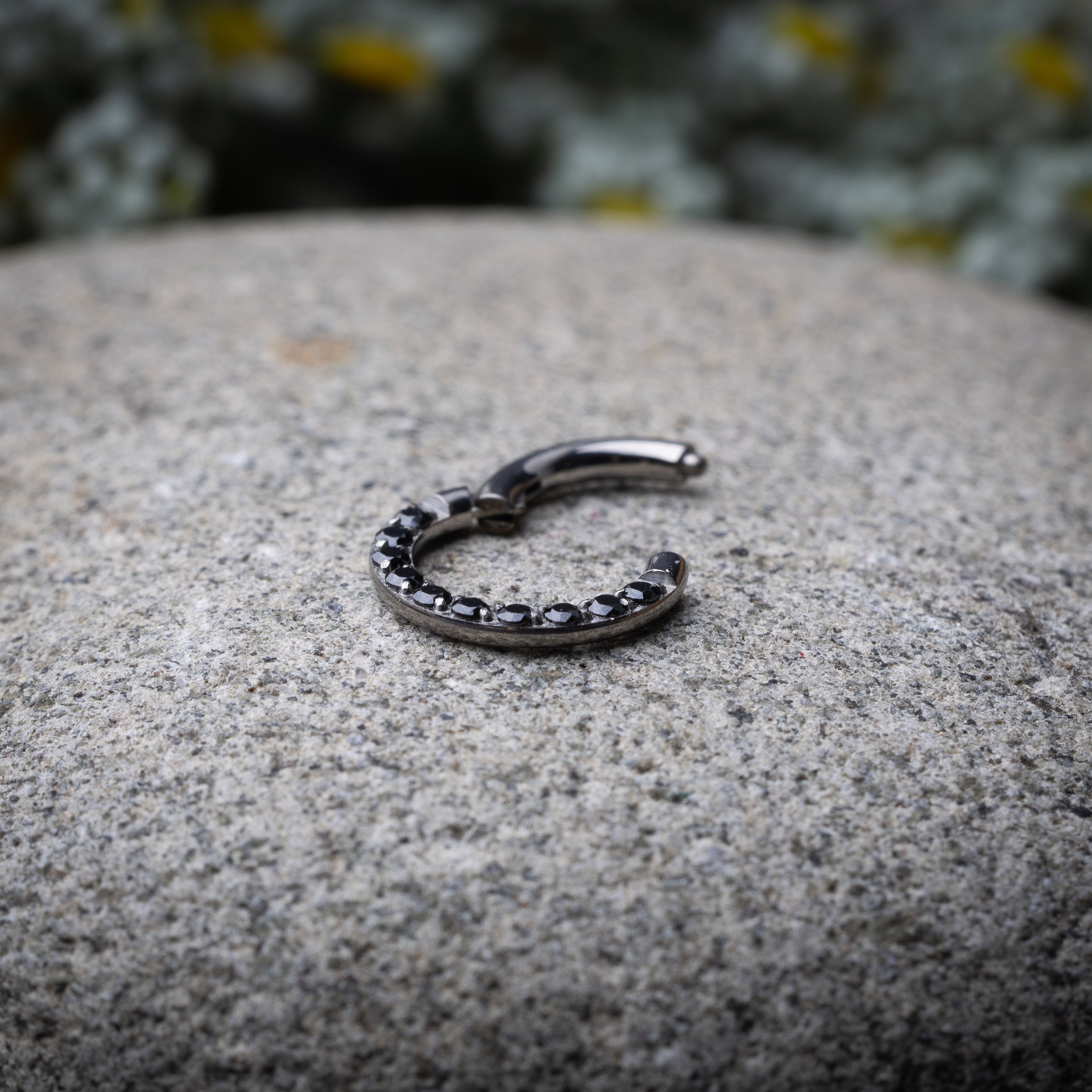 Titanium septum clicker with black gemstones, displayed on a textured dark background.