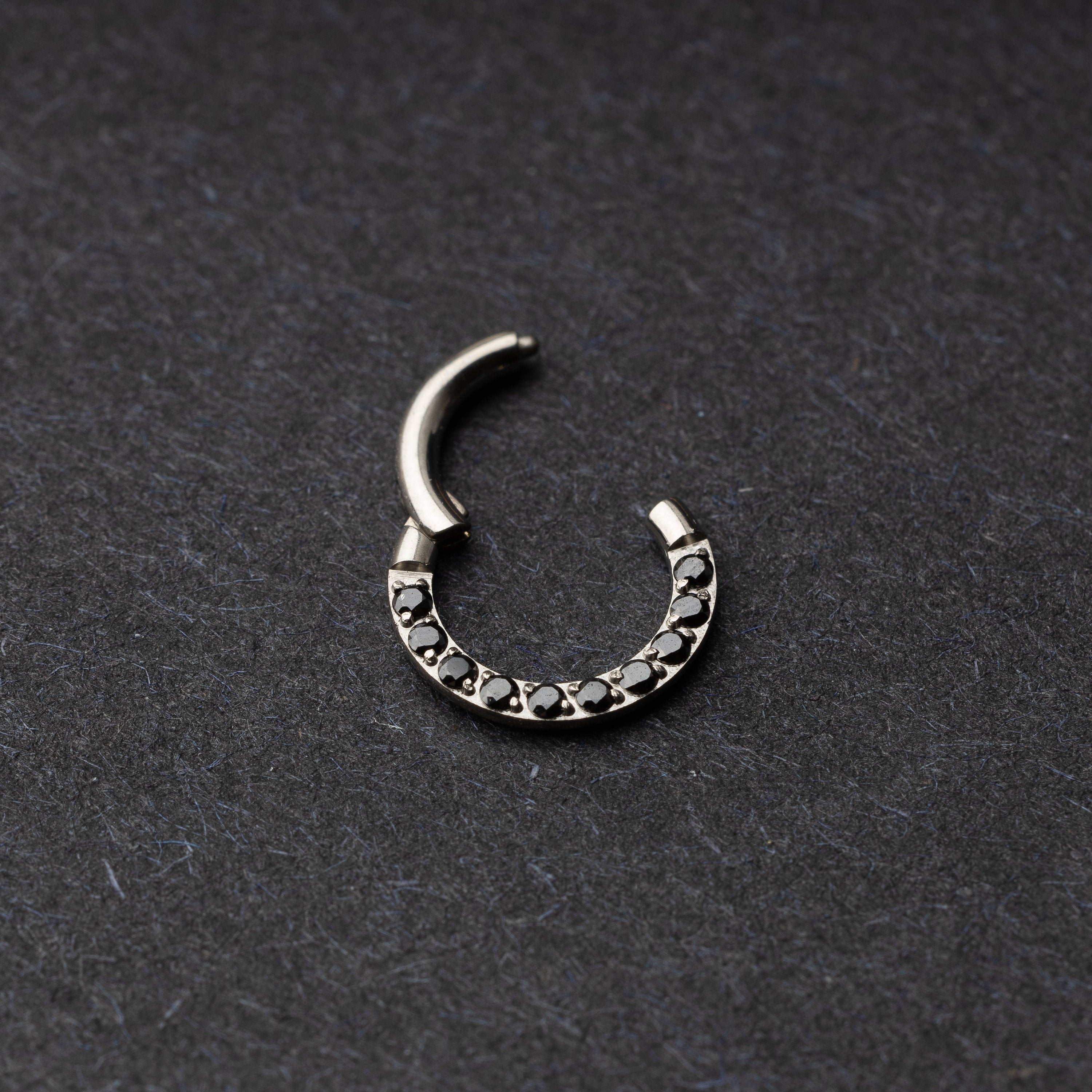 Titanium septum clicker with black gemstones, displayed on a textured dark background.