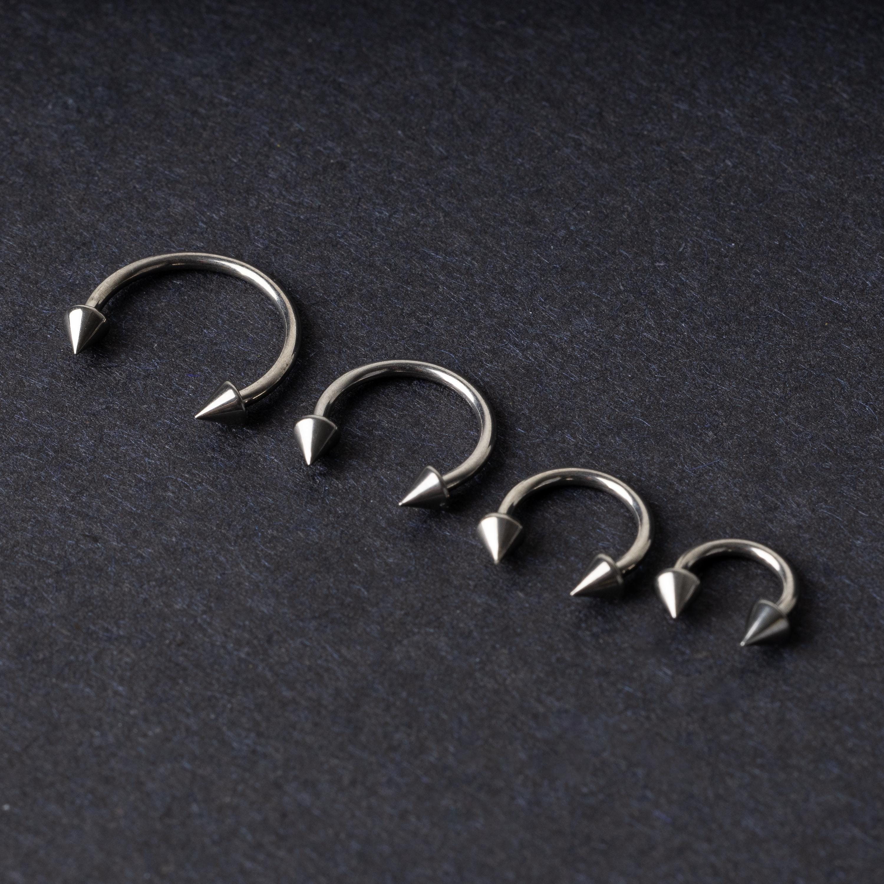 Four titanium horseshoe hoops with pointed cone ends, lined up on a dark background.